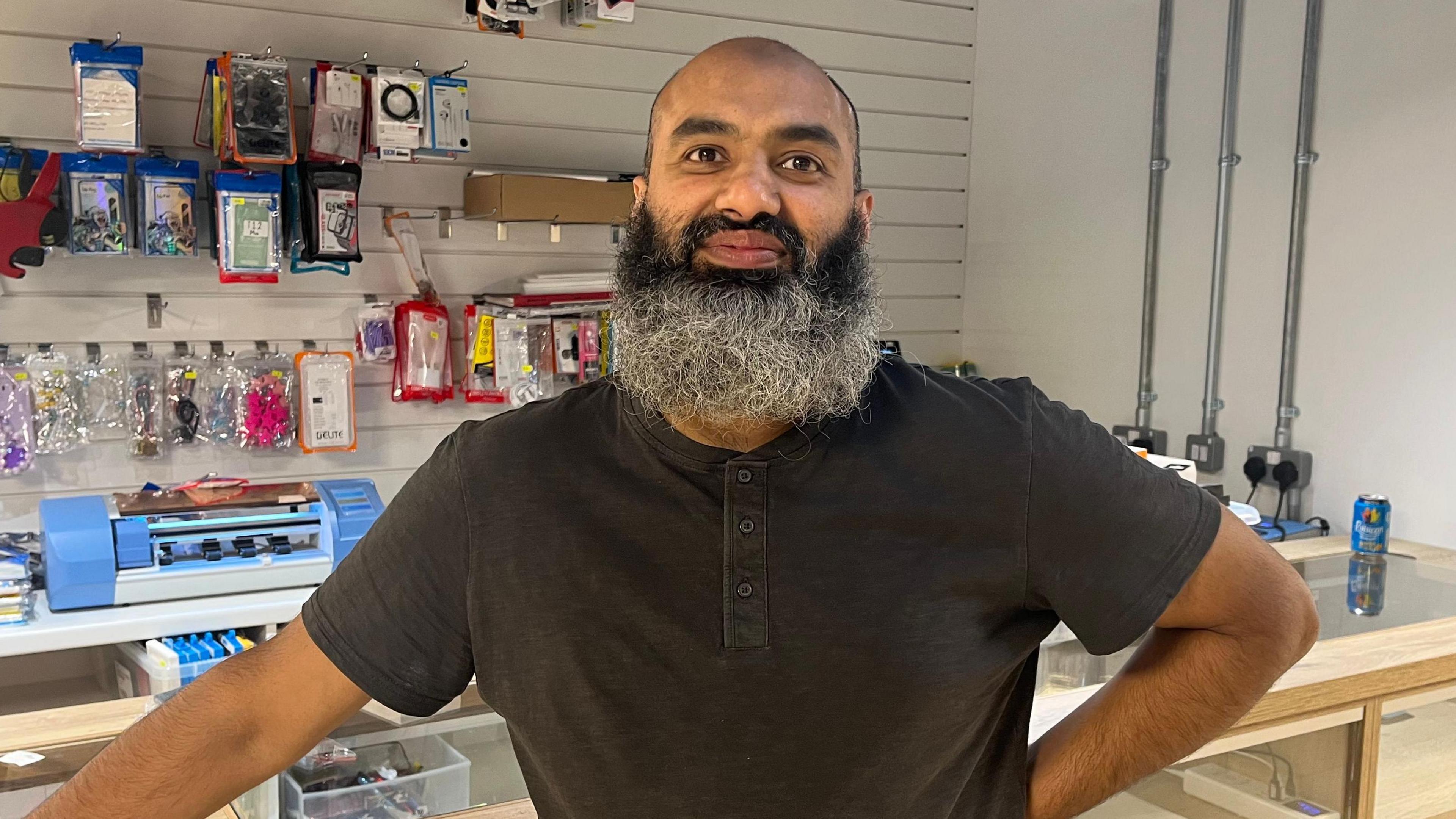 Man with long beard standing in front of mobile phone repair shop.