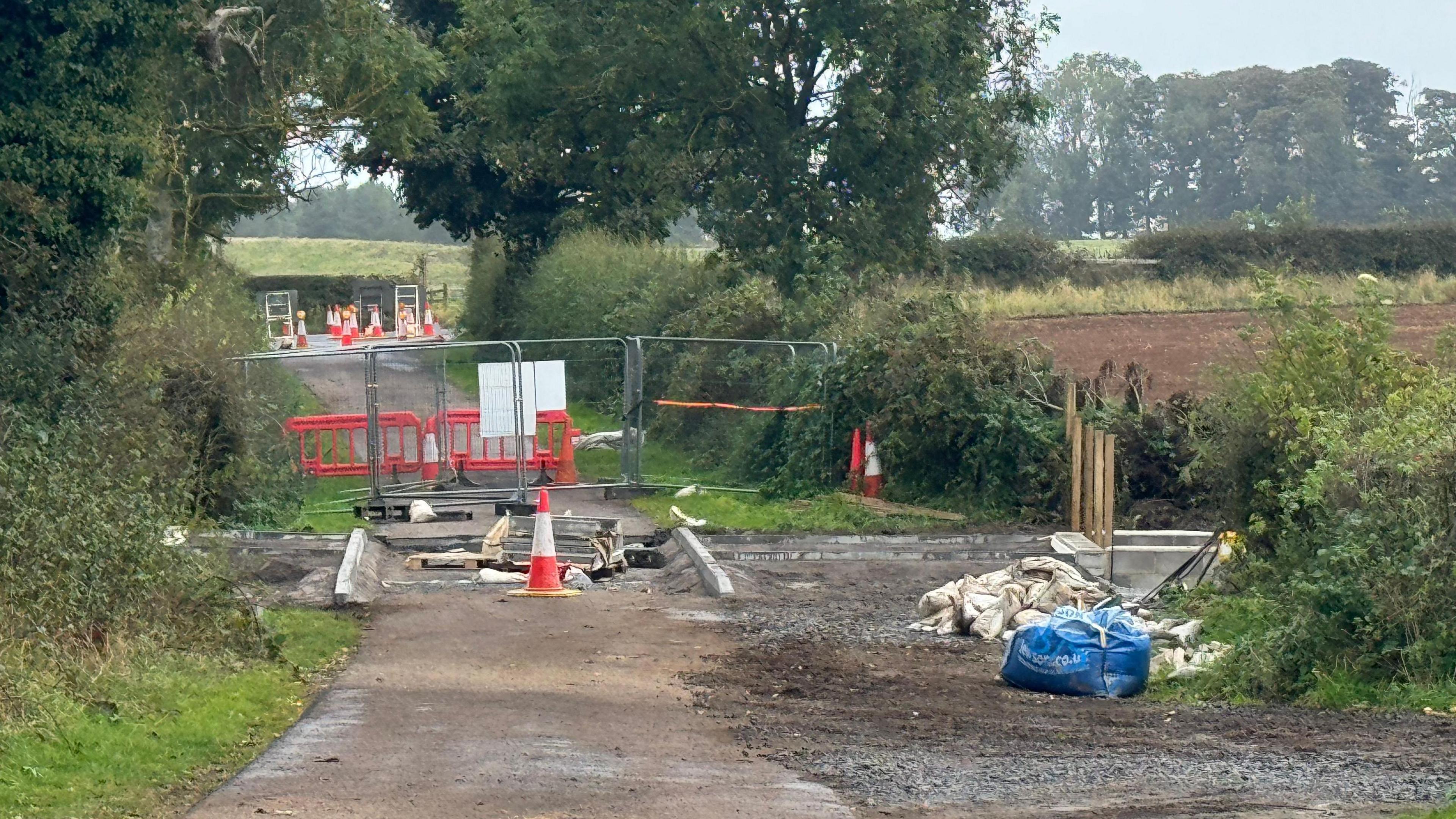 Roadworks on a country road, with metal fences and traffic cones barring off access.