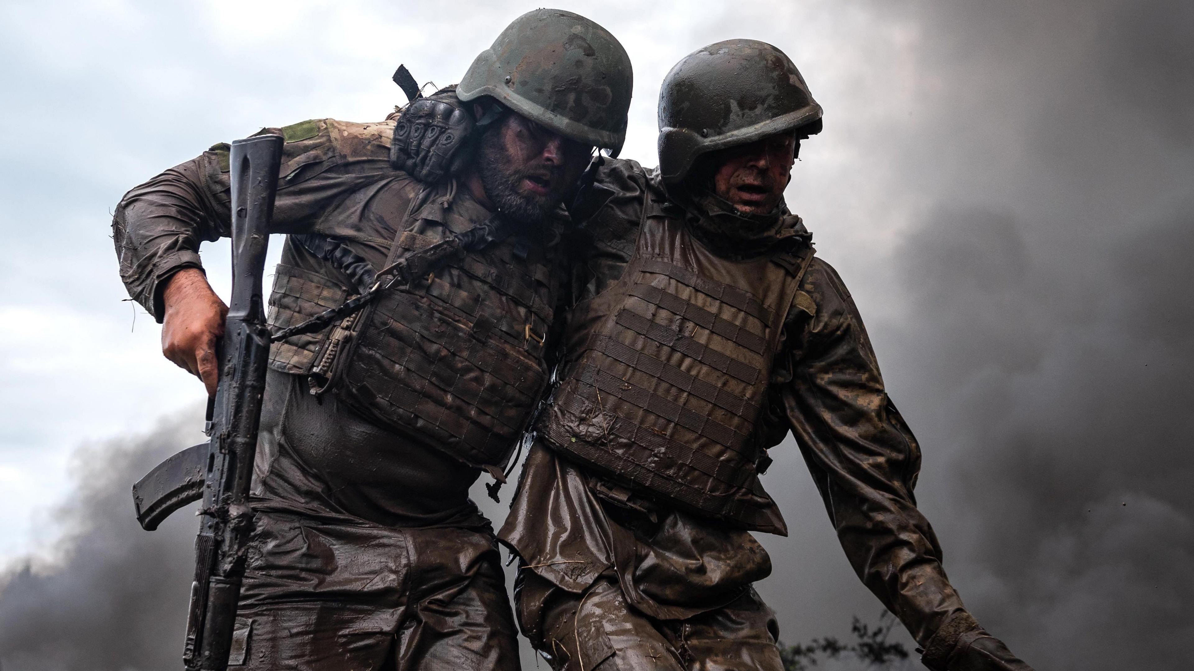 A soldier helps another soldier walk during combat