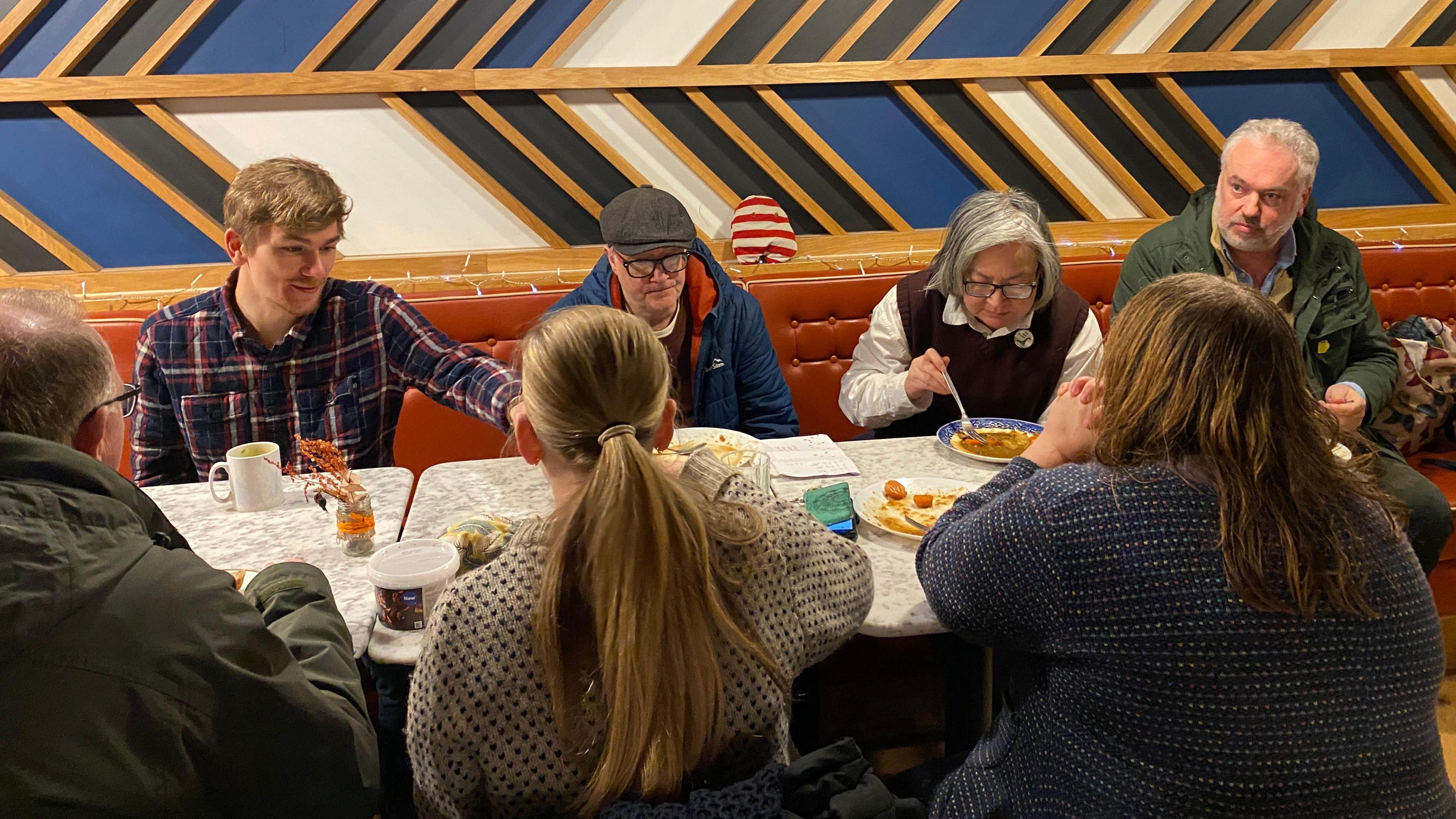 A group of people are sitting around a marble table and eating soup.