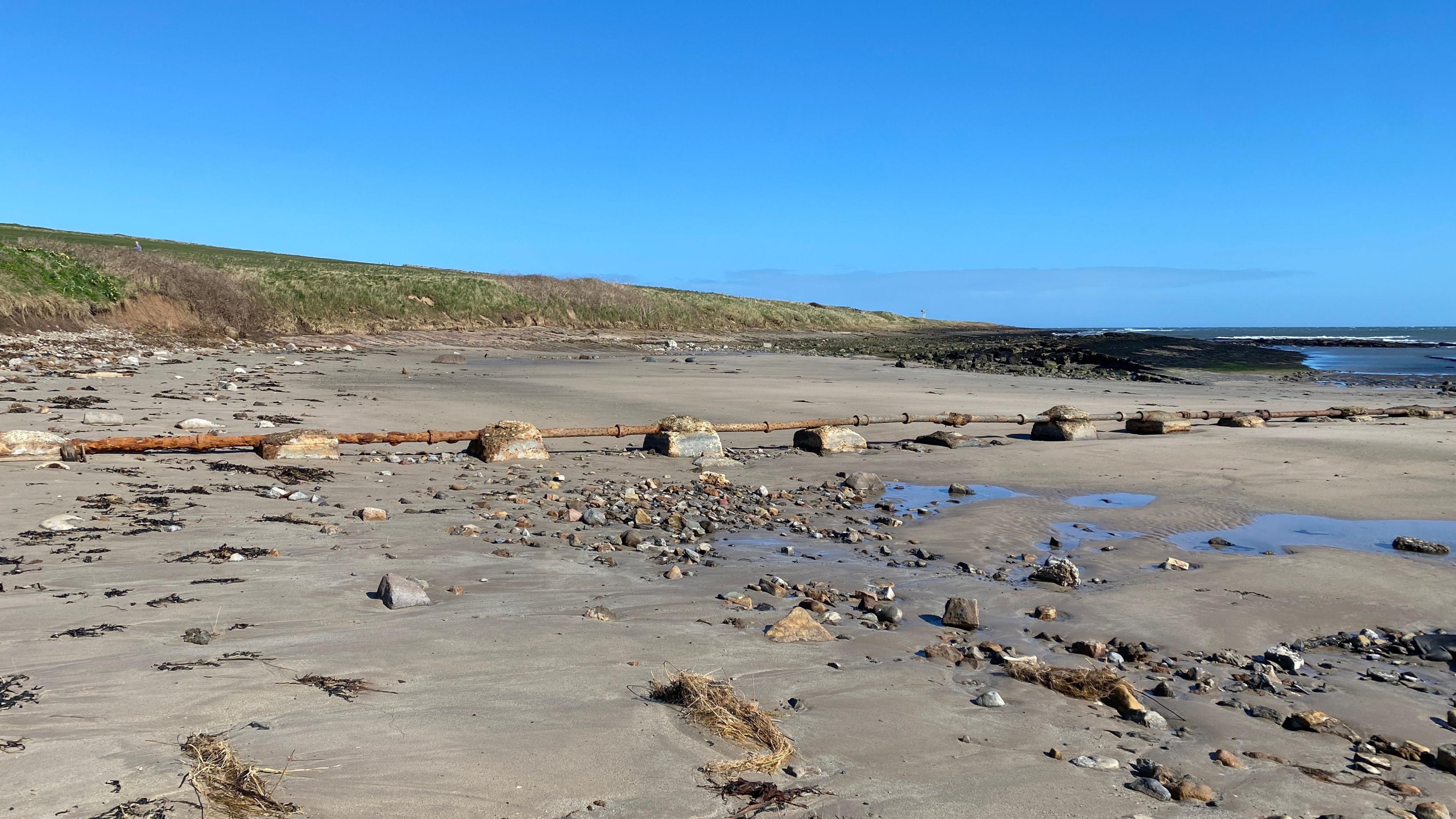 A rusty pipe stretching across the beach into the sea