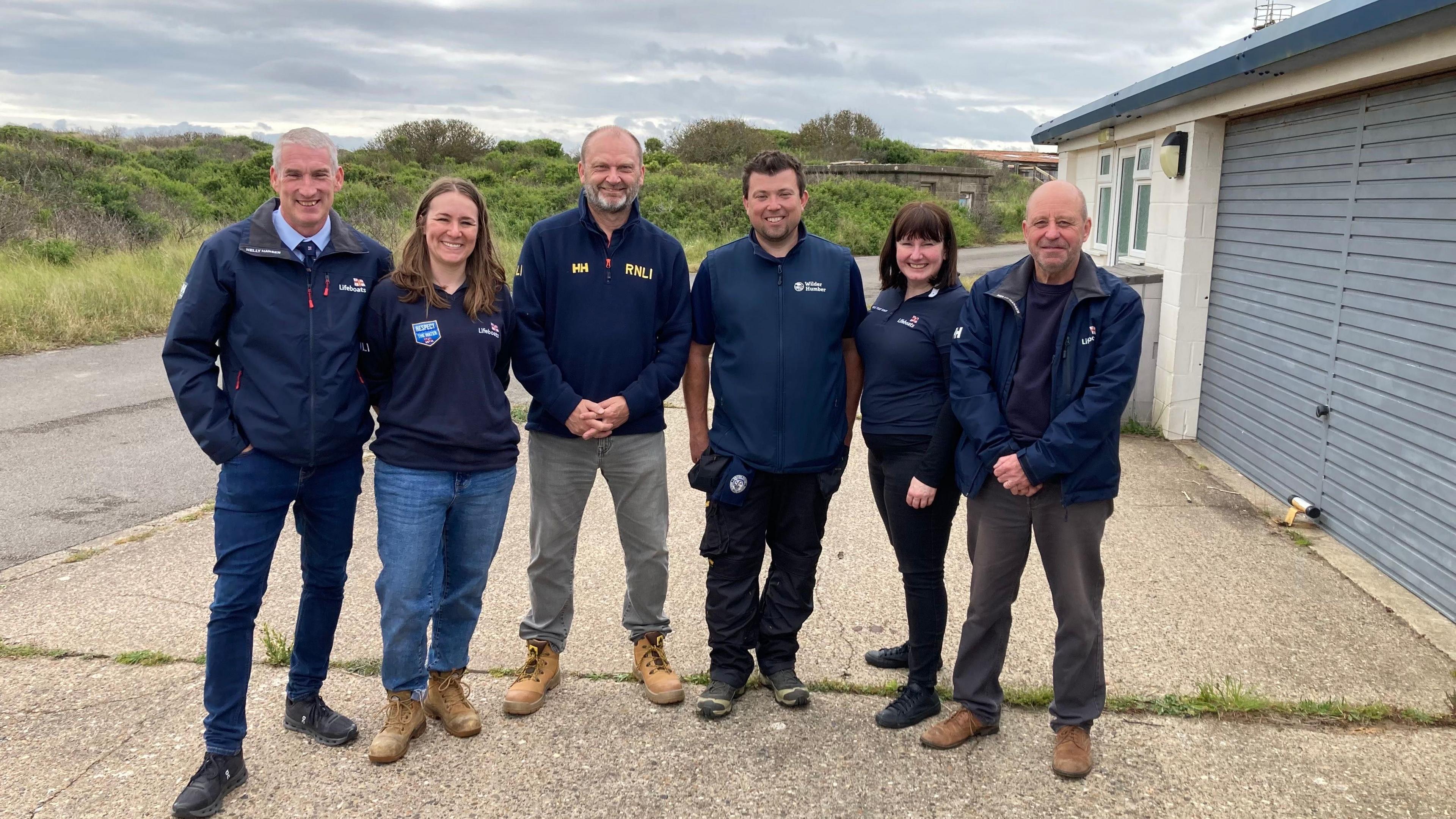 Four men and two women from the lifeboat crew at Spurn Point. They are standing outside the former station in RNLI dark blue branded clothing. 