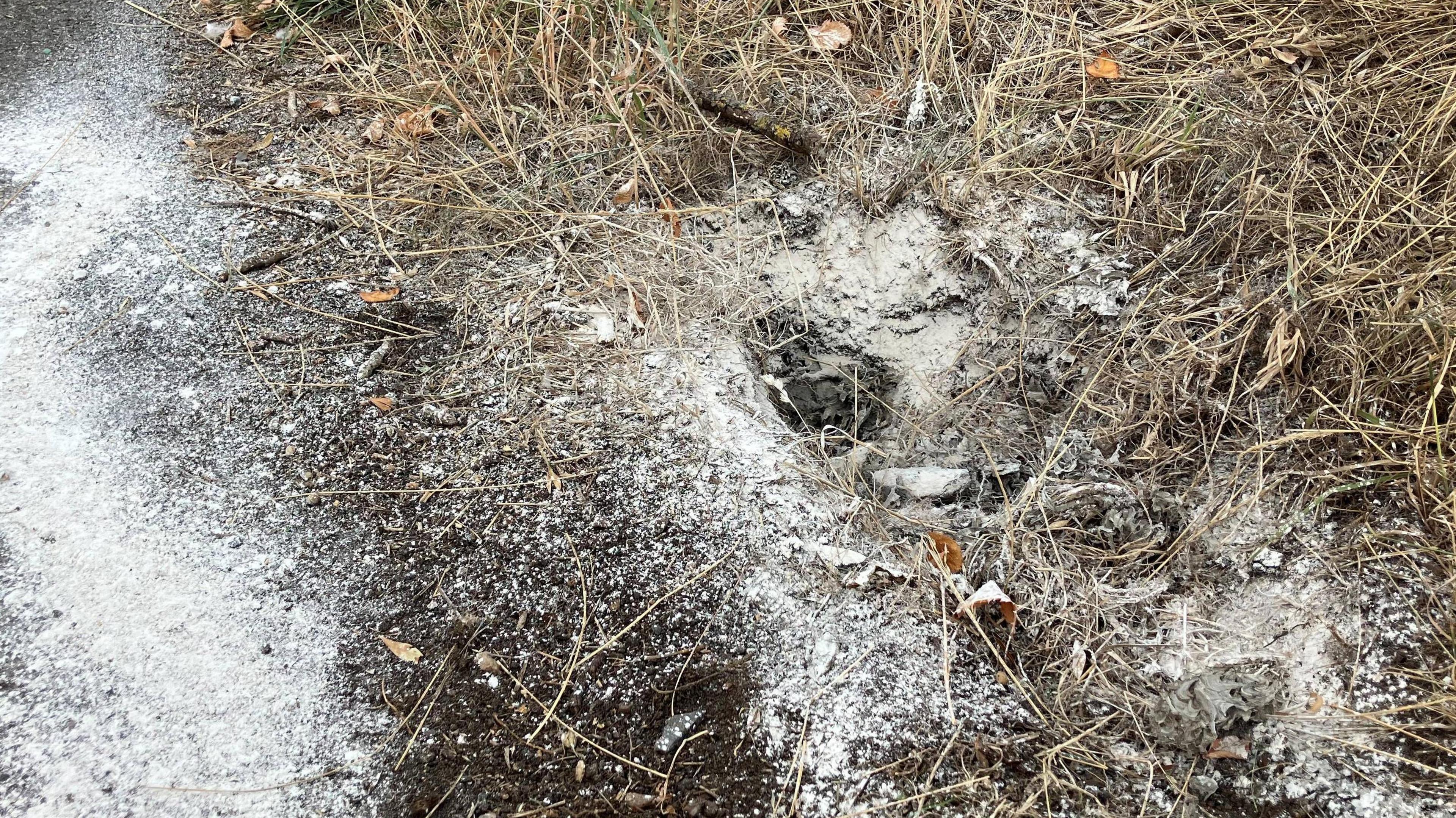 Hole in ground covered in white powder and grass.