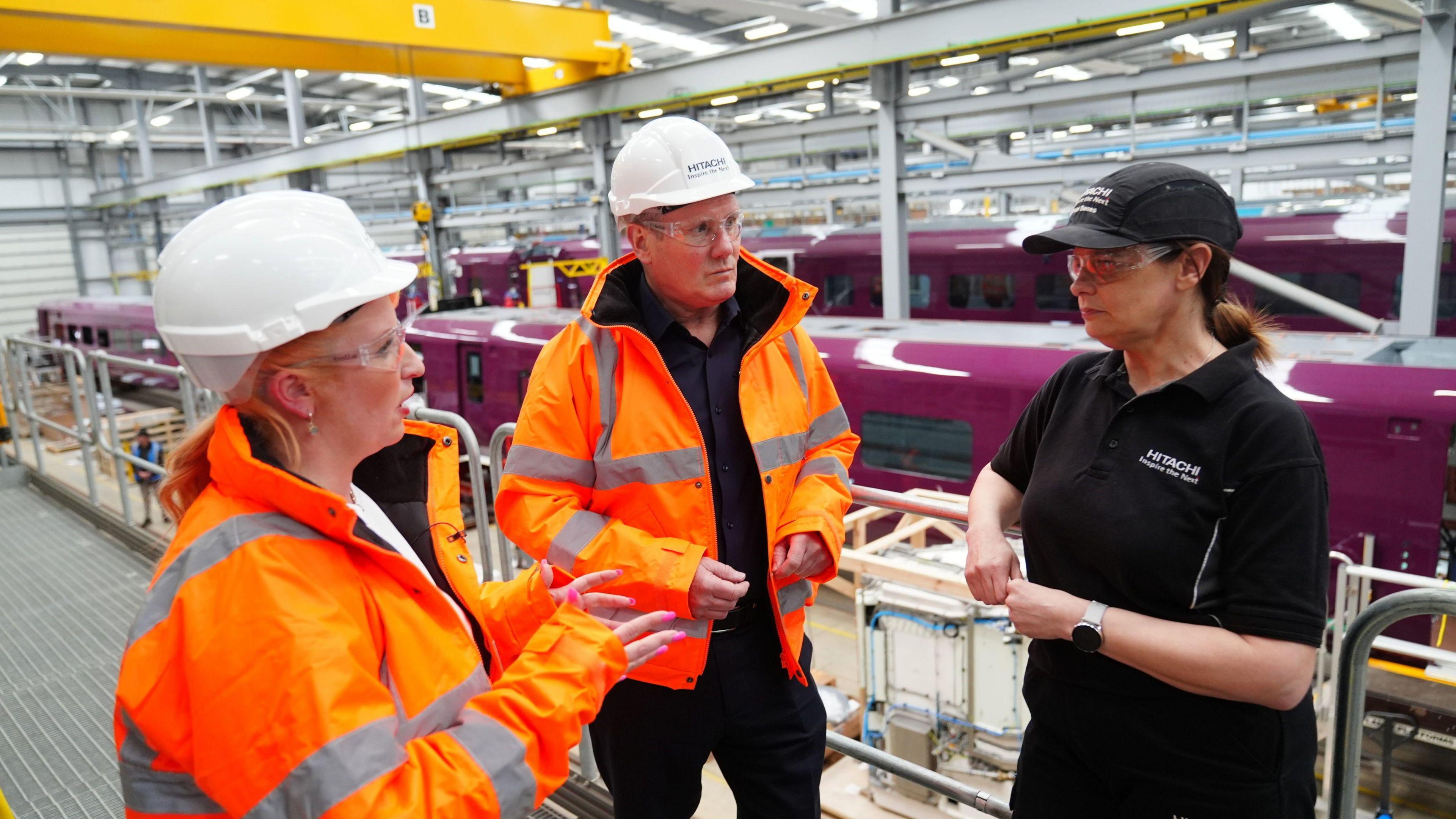 Keir Starmer and Lou Haigh speaking to a worker at the Hitachi factory in Newton Aycliffe. Half-built trains can be seen in the background.