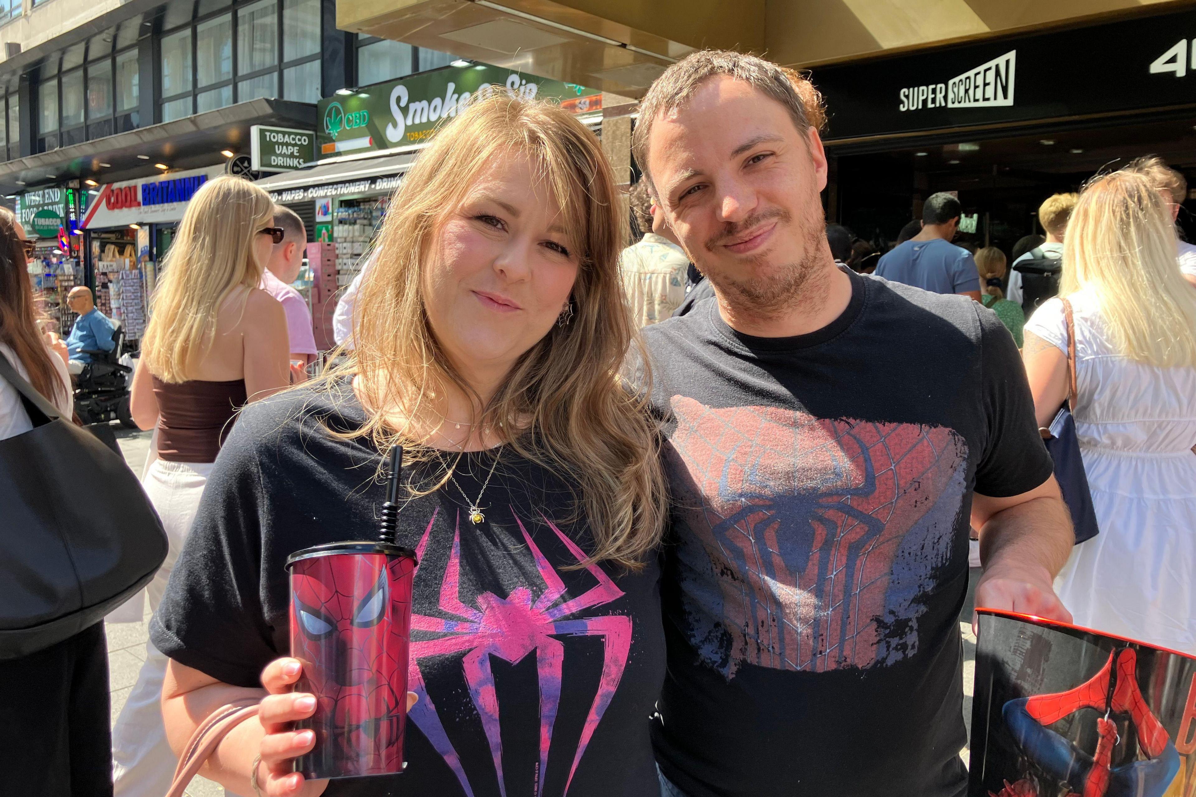 Two Spider-Man fans stand outside a cinema. Both are wearing Spiderman T-shirts and holding related merchandise