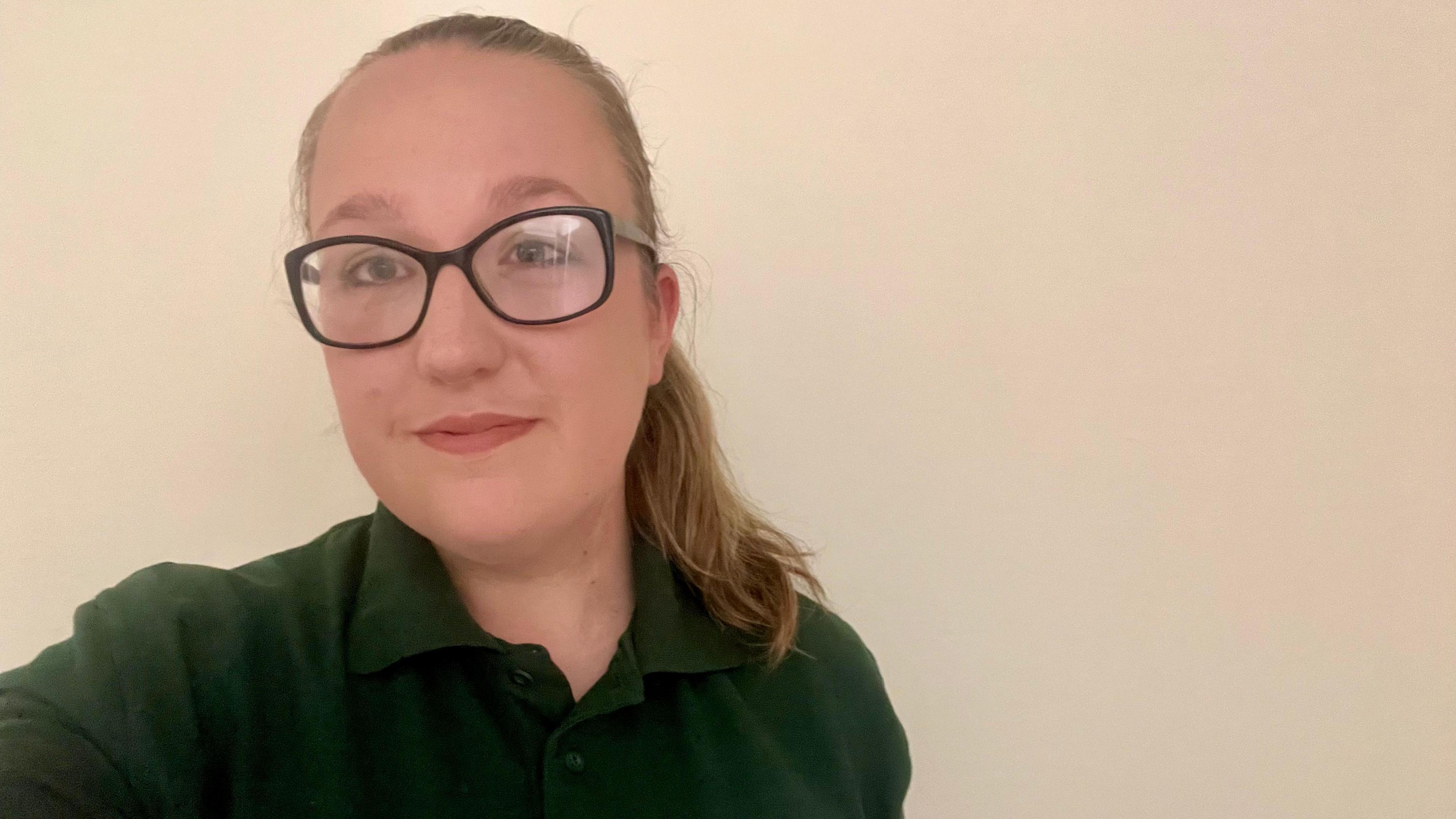 Selfie of Georgia Taylor who has her air in a ponytail and is wearing glasses and a green polo shirt