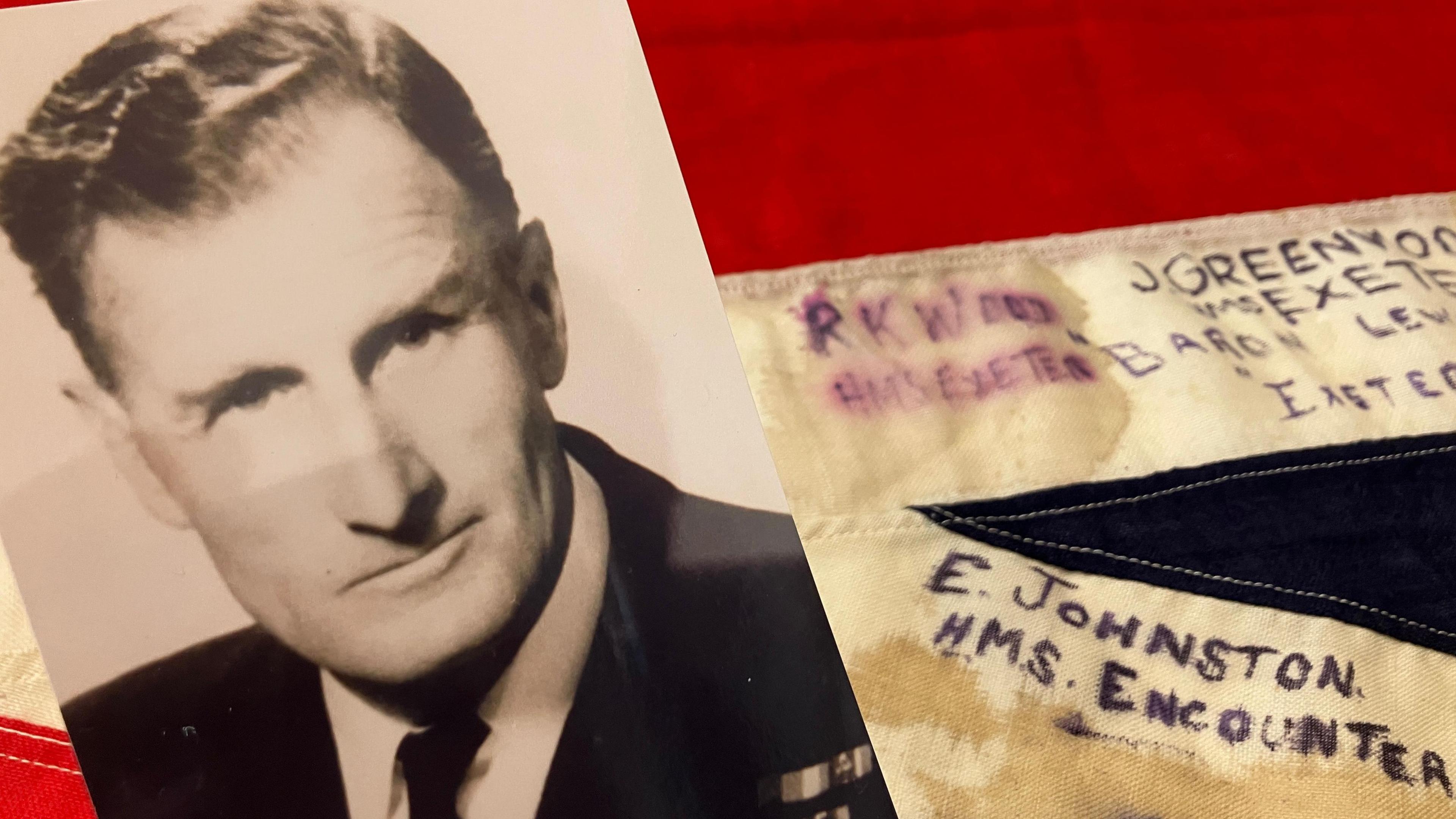 A black and white picture of Richard K Wood in naval uniform alongside a uion flag with names written on in capitals