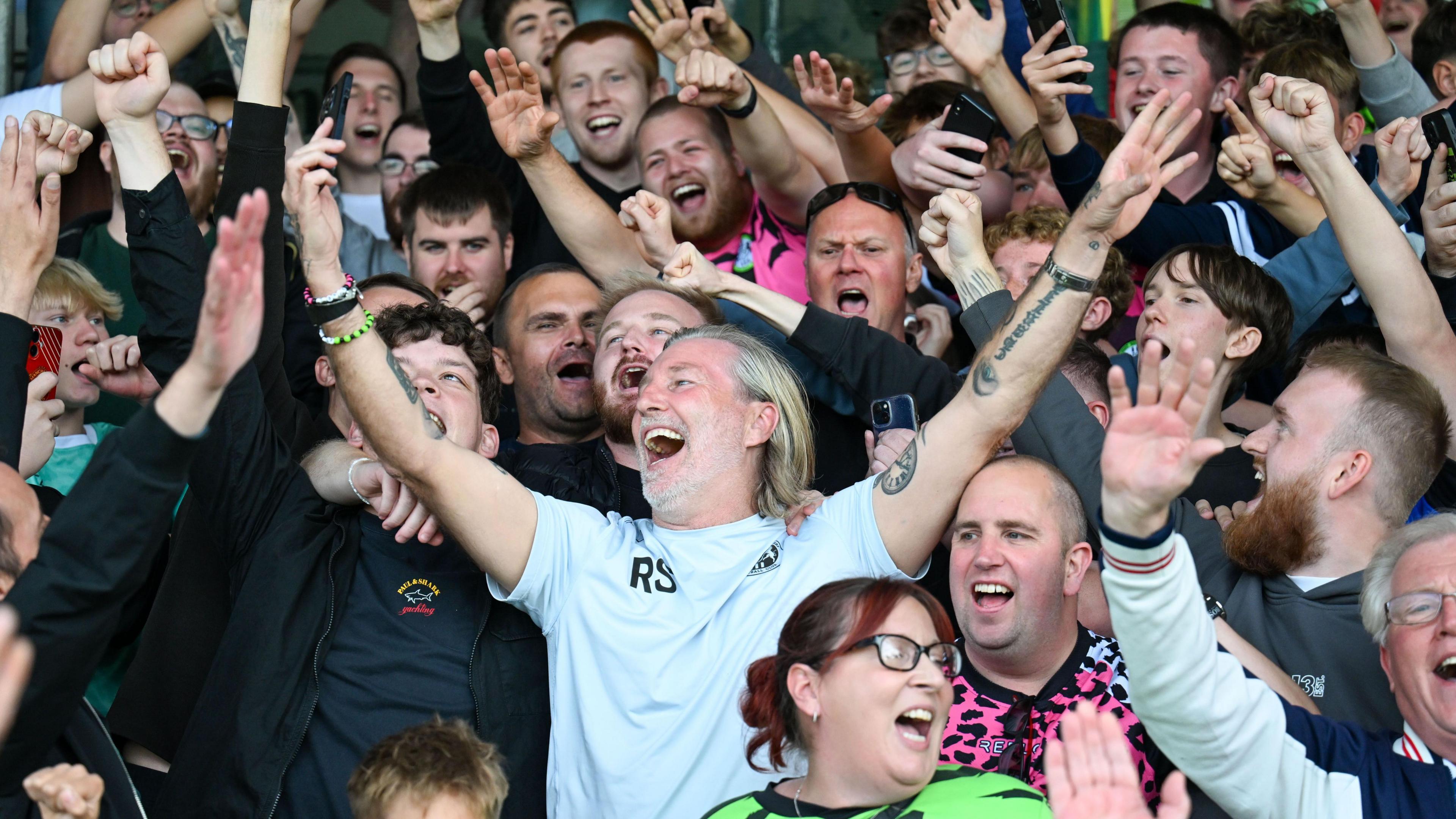 Robbie Savage (centre) holds his arms in the air above his head surrounded by fans in the stand