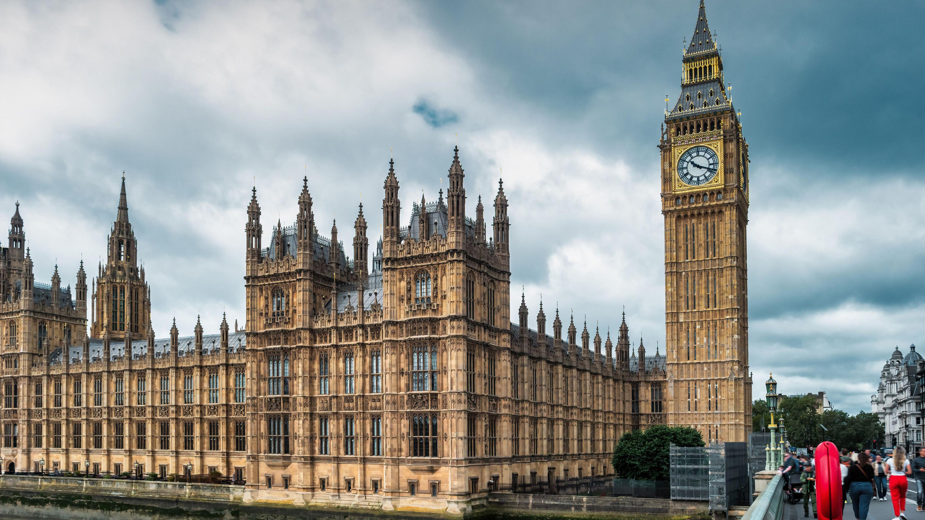 General view of the Houses of Parliament in London, with clouds and grey skies overhead. Palace of Westminster and Big Ben clock face.