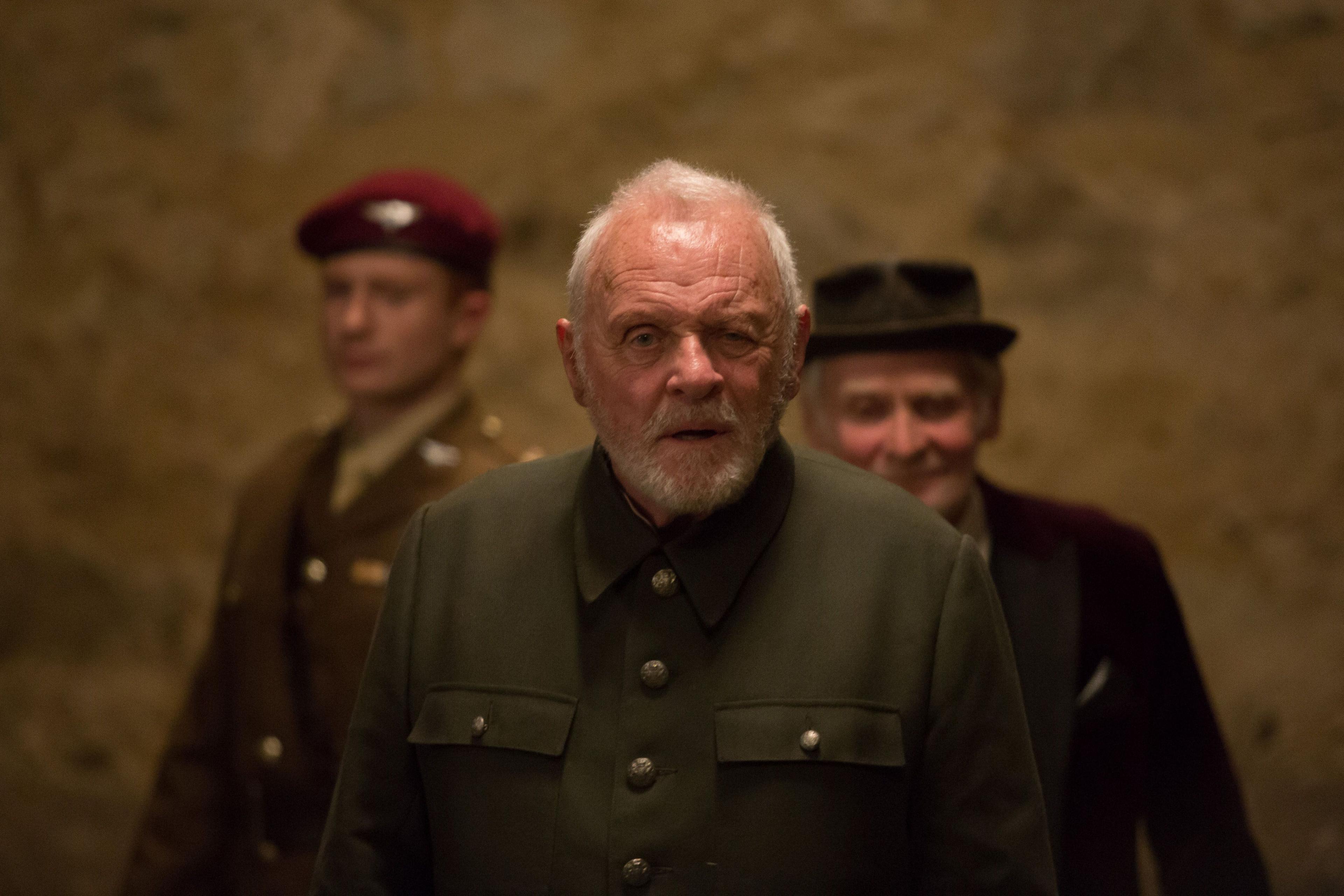 Sir Anthony in khaki jacket with gold buttons. Grey hair and white beard looking haunted. Two men behind either side of him.