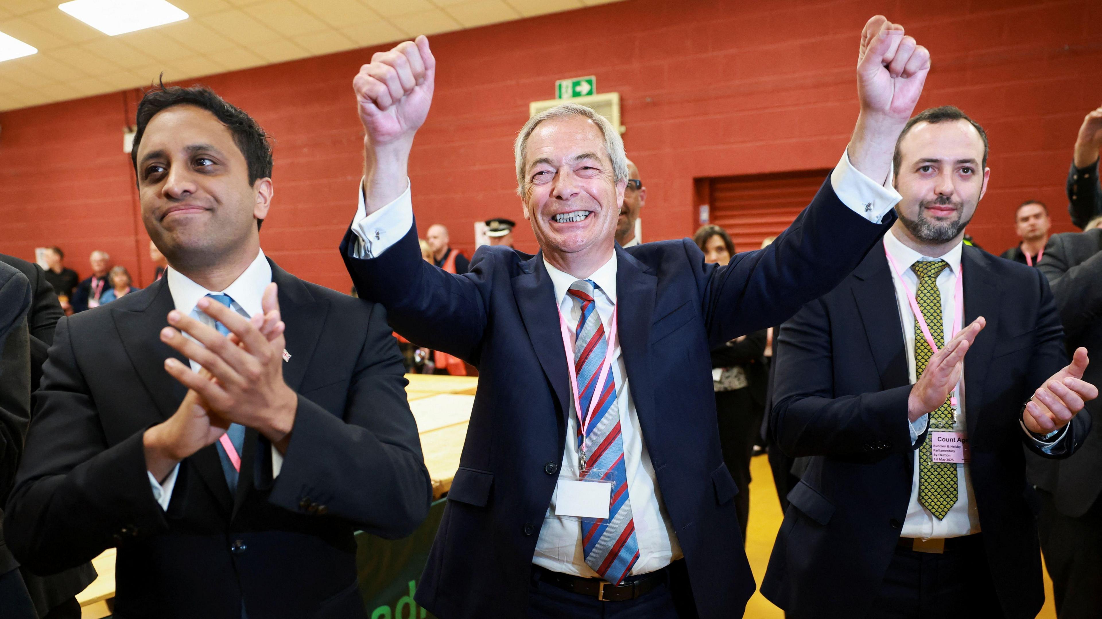 Nigel Farage celebrates with his fists in the air, alongside Reform UK chairman Zia Yusuf.