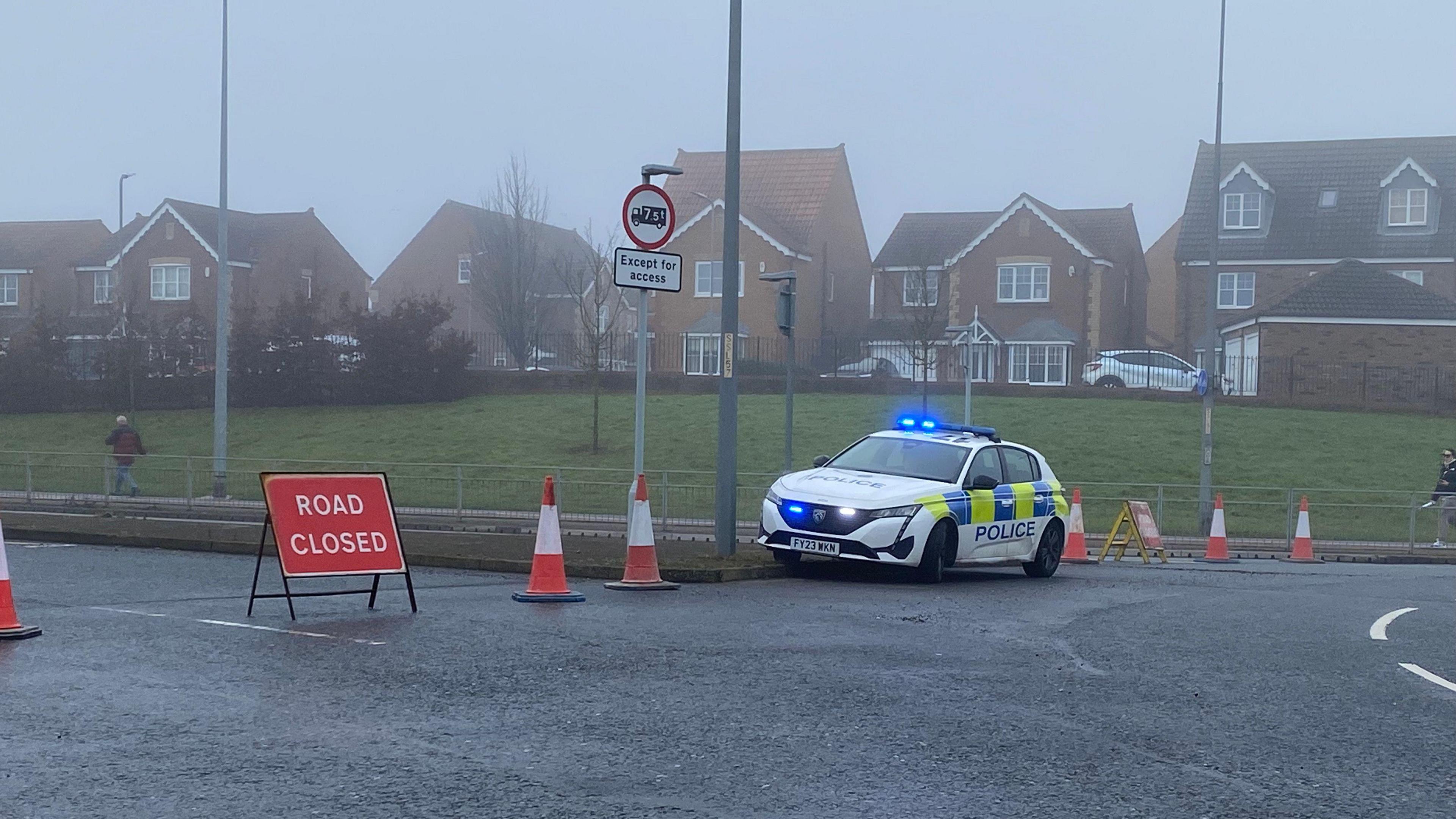 A police car parked by a closed road