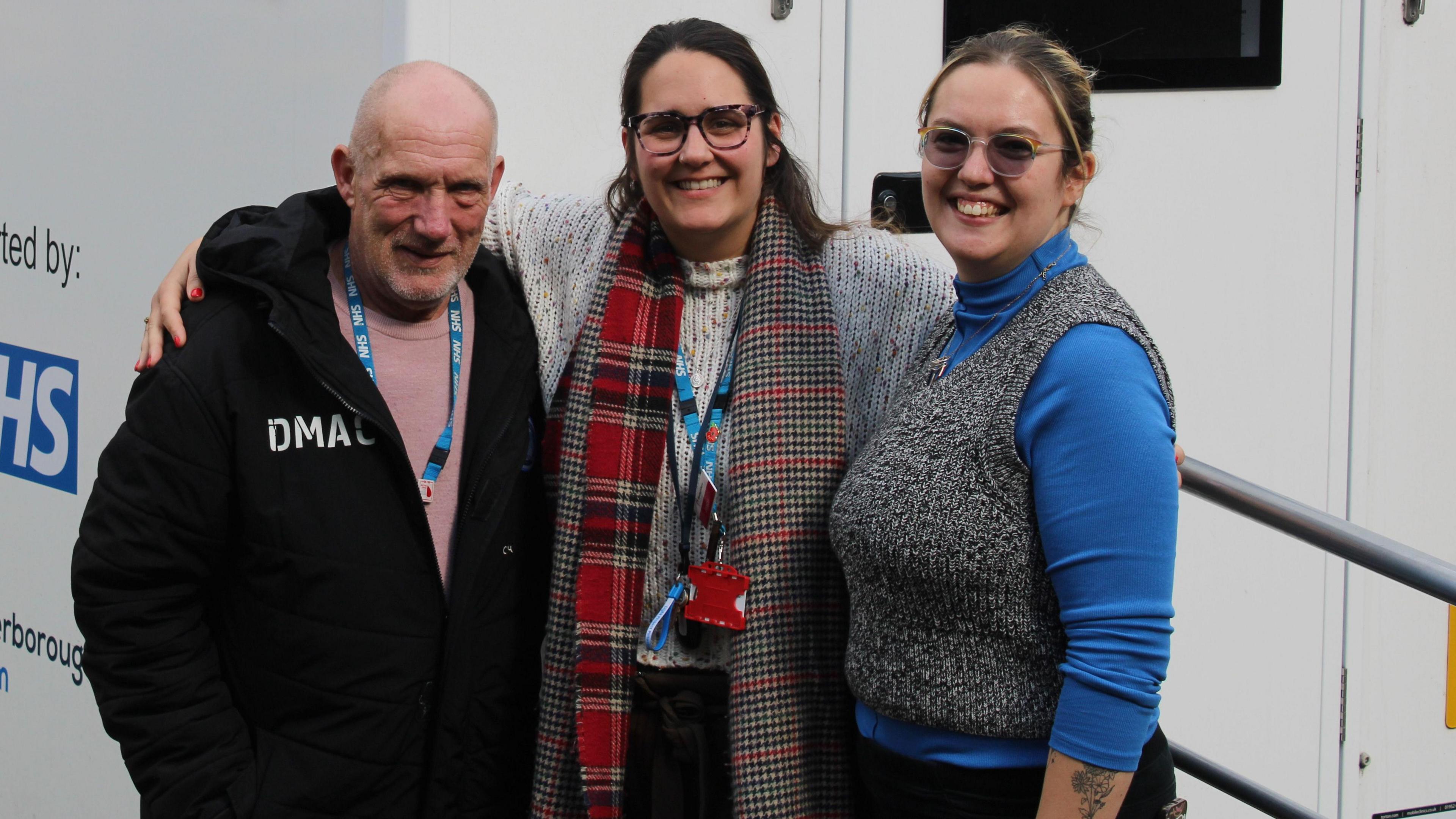 Roy wearing a black coat standing next to Jess wearing a checked scarf and grey sweater and Heti wearing a blue jumper and a grey waistcoat, from the Boroughbury outreach team 