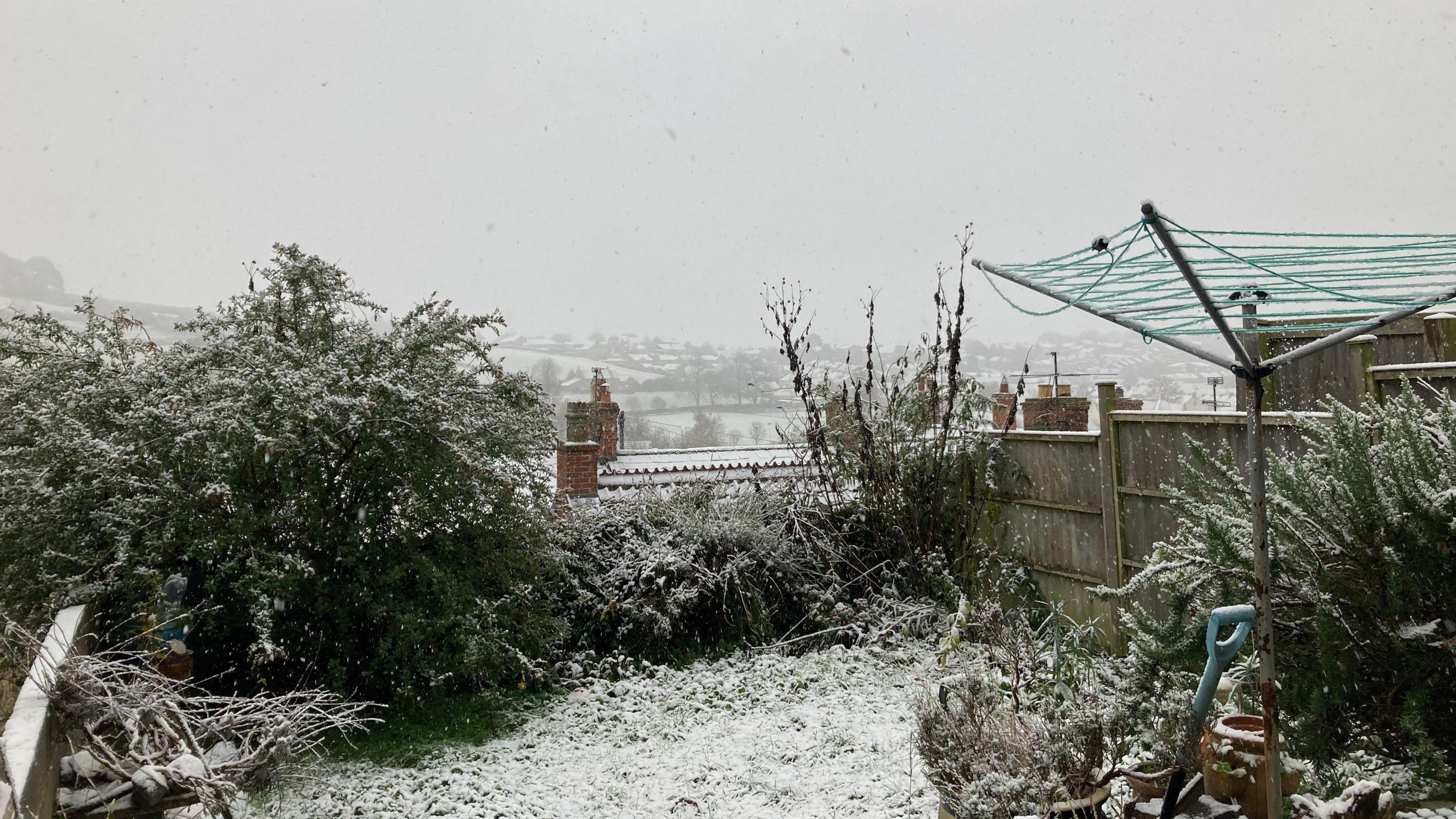 A snowy garden in Ilminster with a drying rack and some bushes. In the distance you can see hills covered in snow.