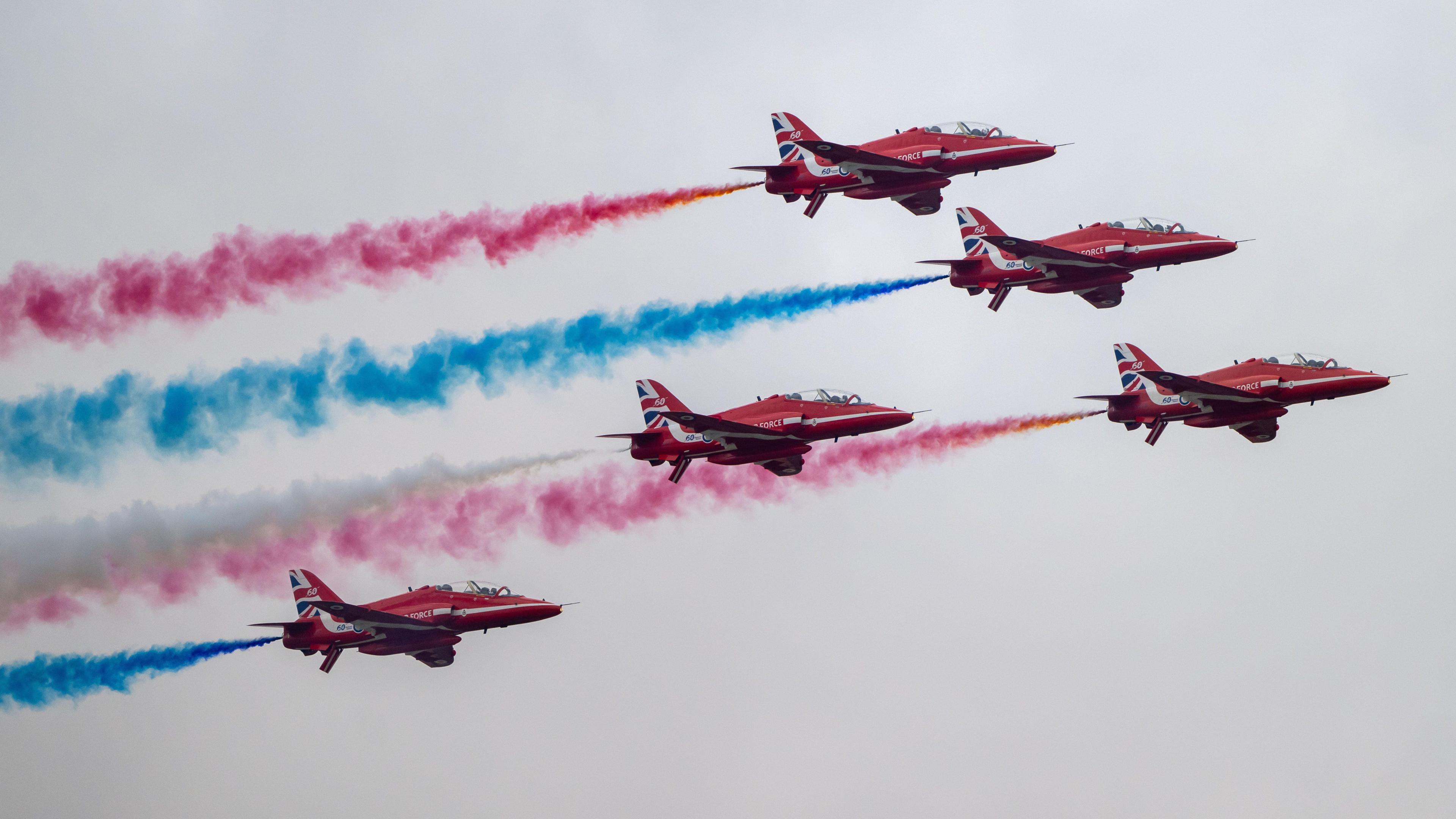 The Red Arrows put on a display at the Royal International Air Tattoo against a gloomy sky, projecting red, white and blue behind them