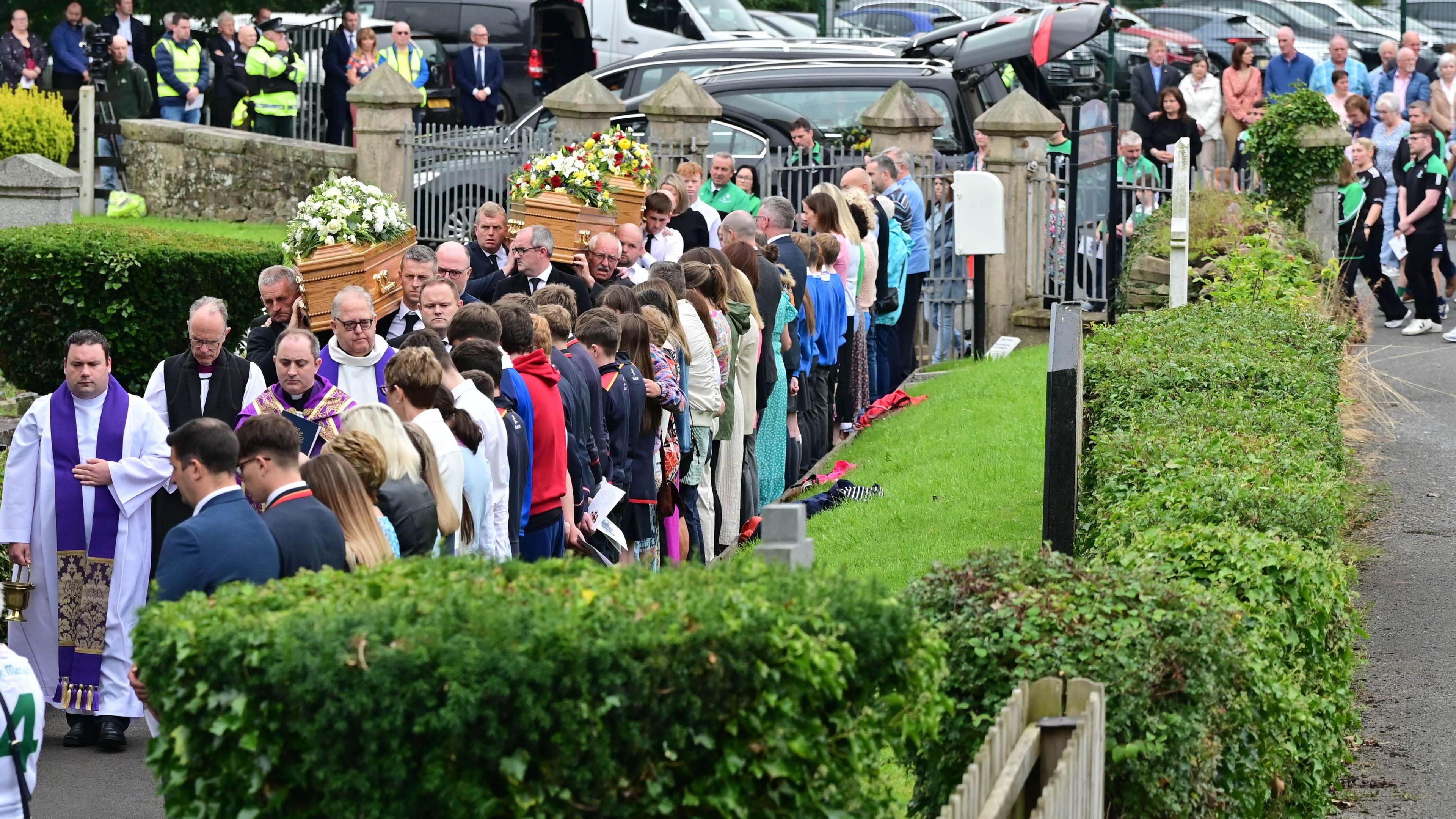 A queue of people outside St Mary's Church in Maguiresbridge. There are a number of mourners carrying the coffins.