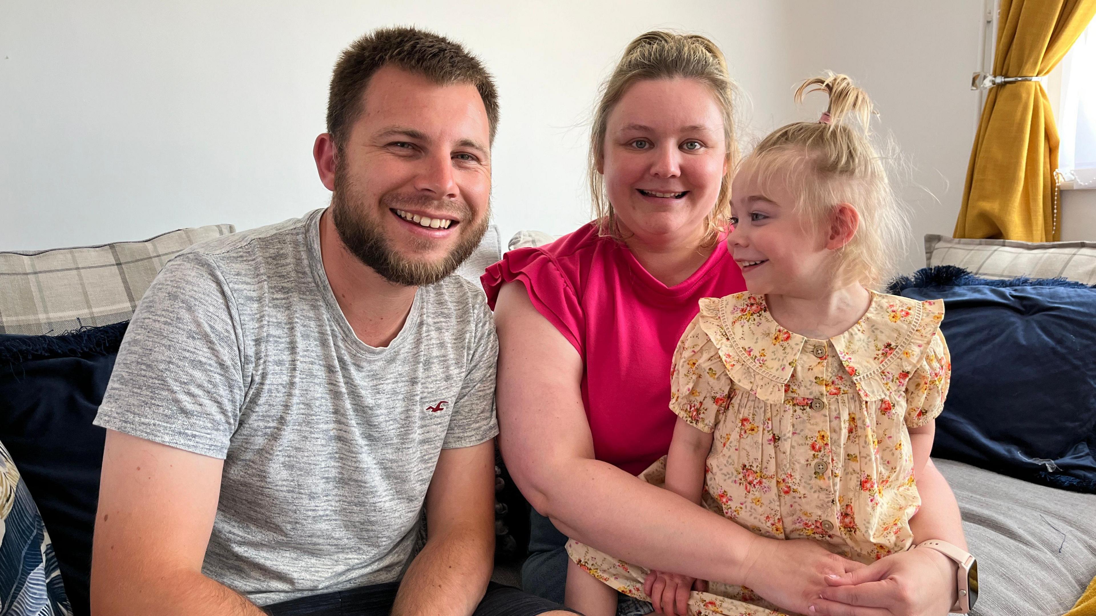 Rich Bolter, Jodie Woolford and Amelia pictured on their sofa with Amelia looking at her parents with a smile