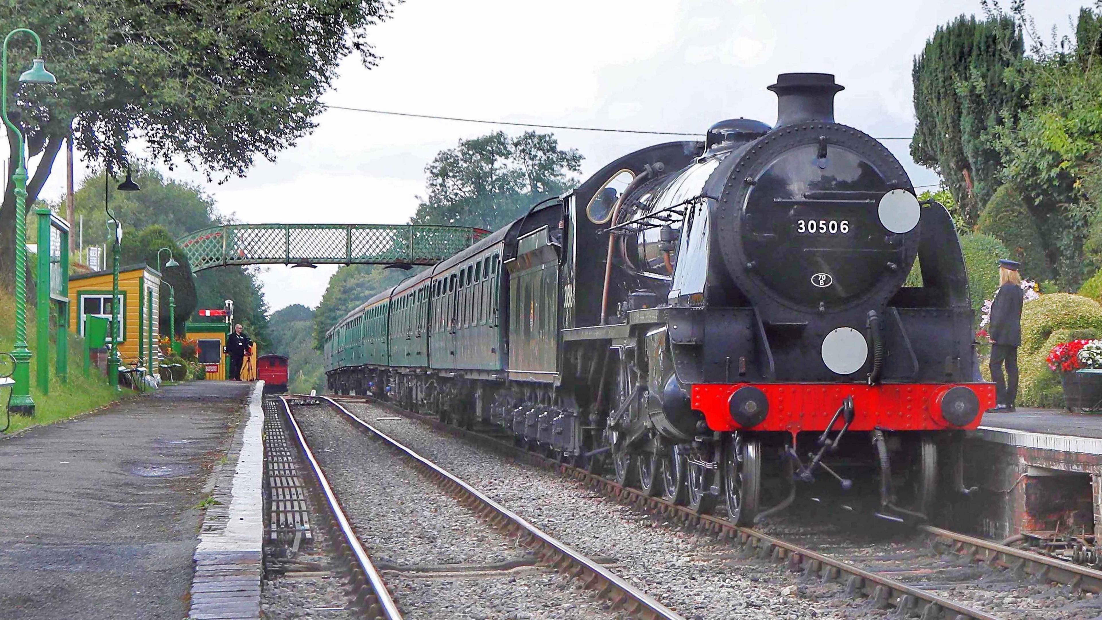 A steam locomotive at an old-style station, with a couple people standing on opposing platforms.