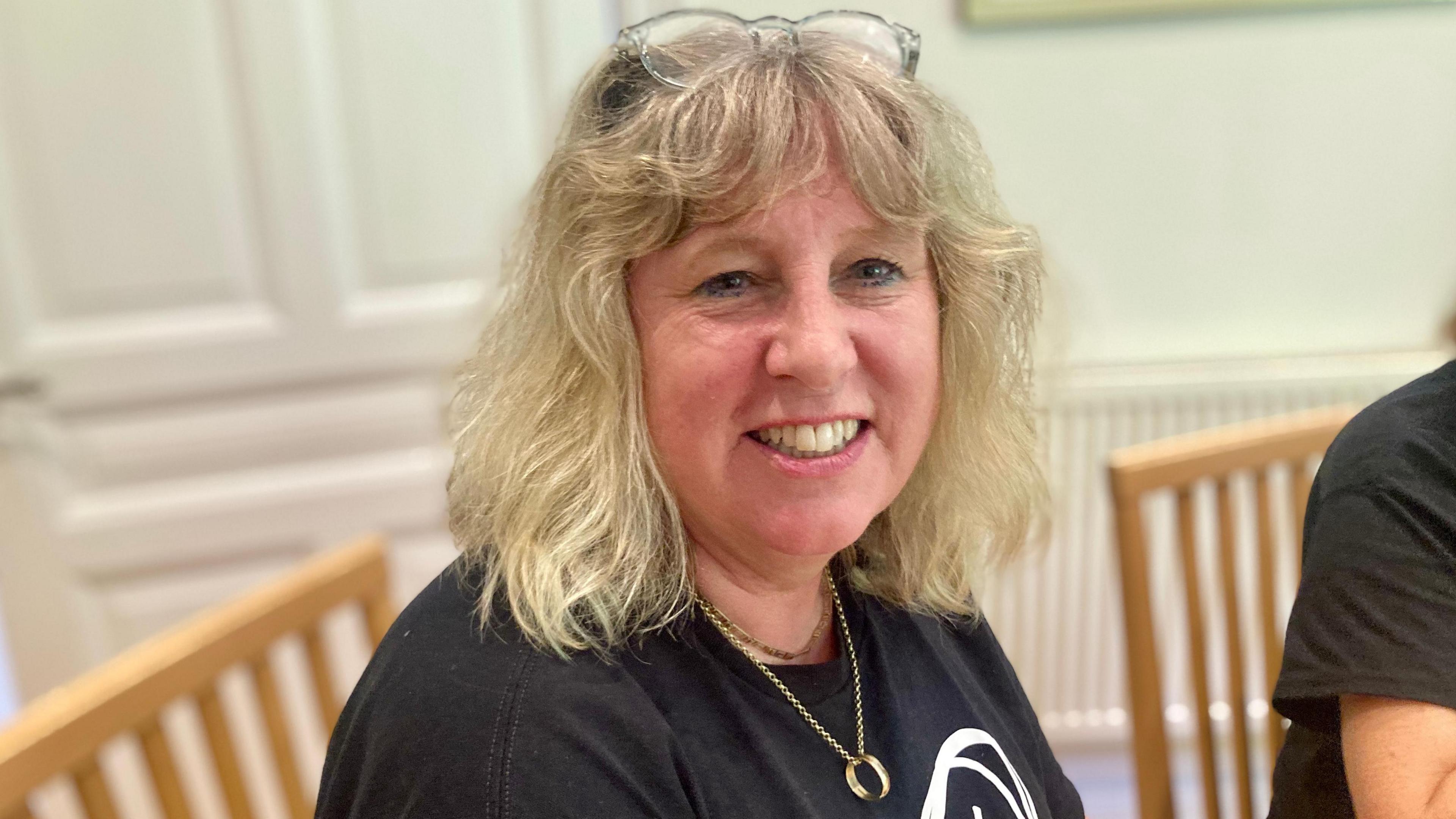 A woman with fair shoulder-length hair with glasses on the top of her head and wearing a black t-shirt