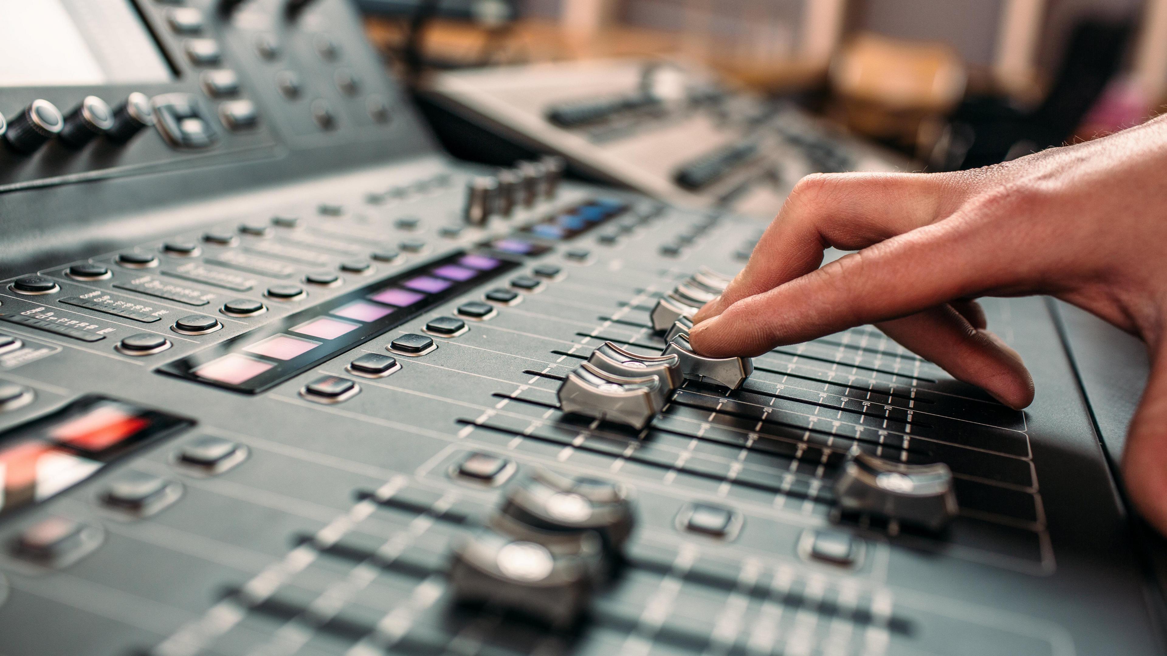 A person's hand moving sliders on a professional high-end sound mixing desk.