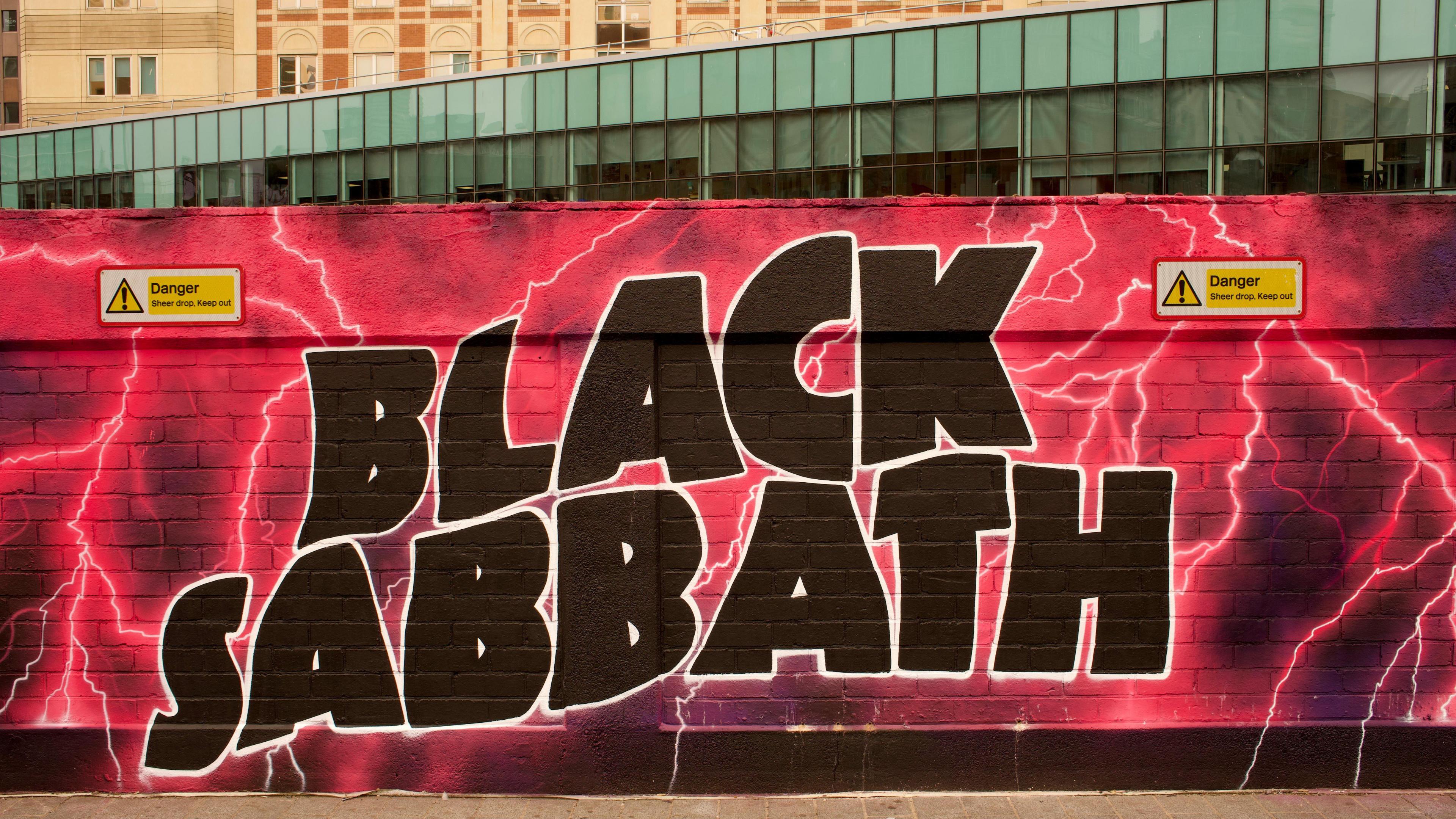 Part of a mural in Birmingham city centre with Black Sabbath in black letters on a neon pink background with streaks of lightning