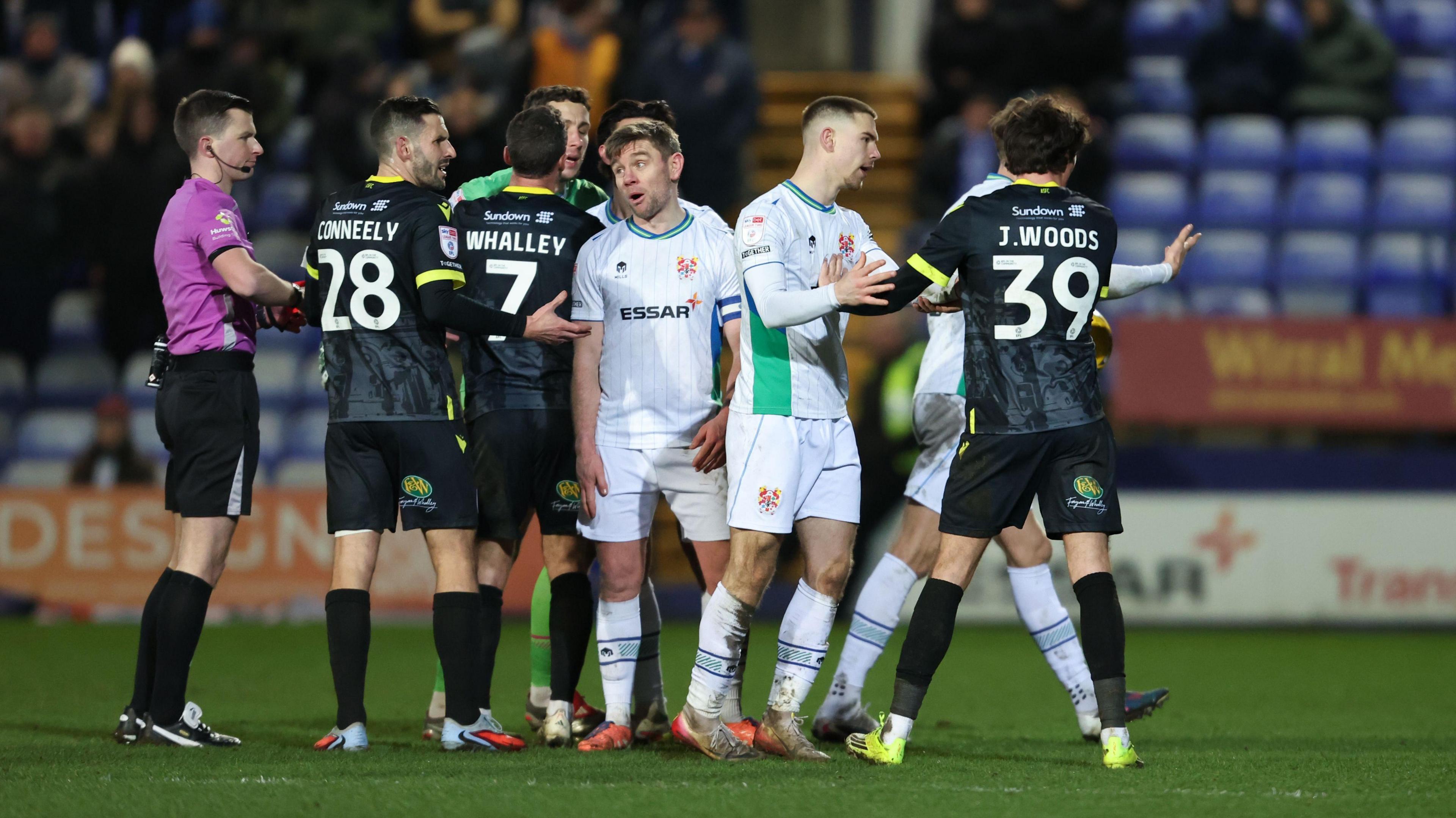 Referee Edward Duckworth (left) stands on the side of a group of Tranmere and Accrington players before sending off Josh Woods