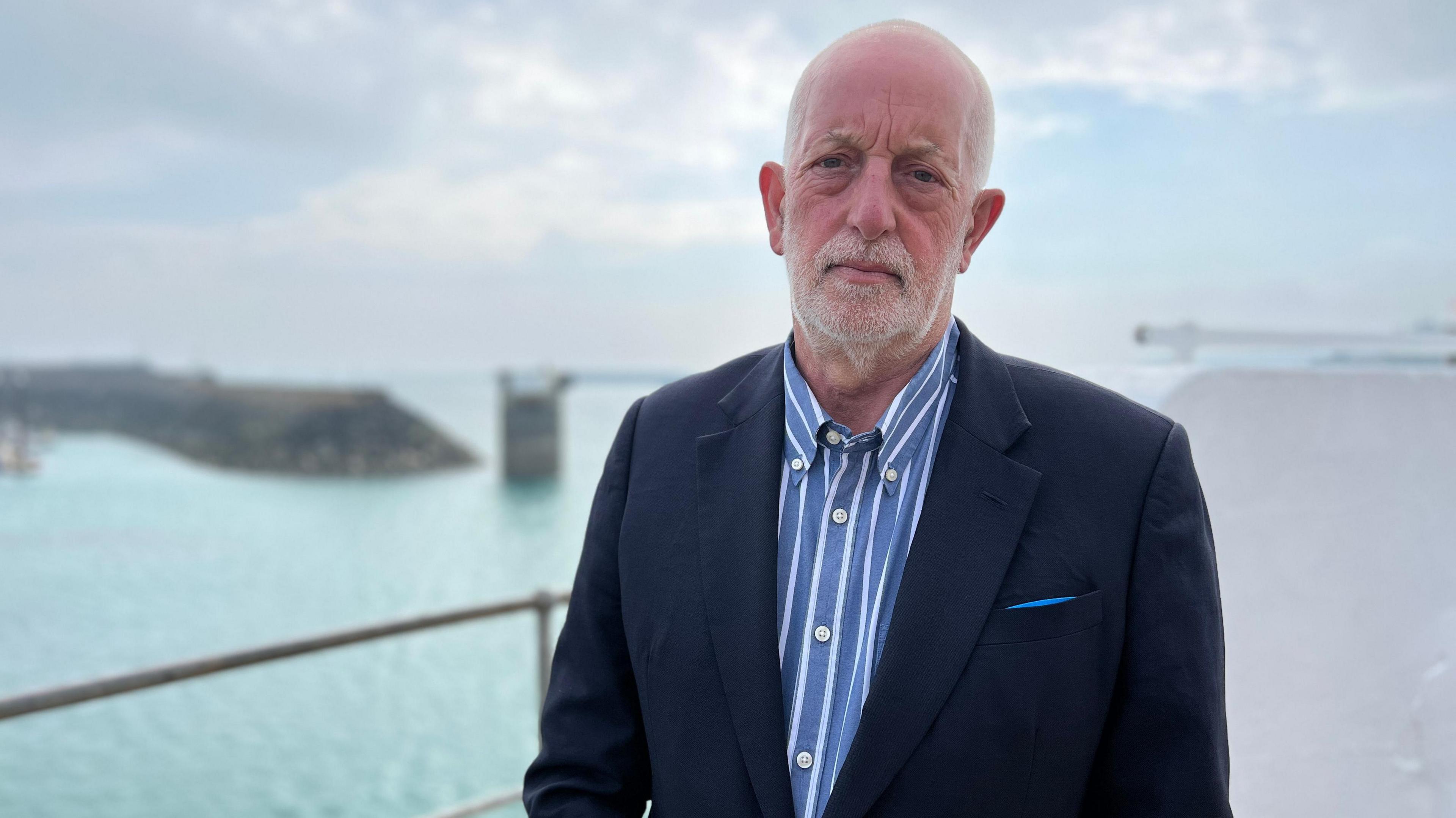 Steve Luce stood by a railing with St Helier Harbour and the sea behind