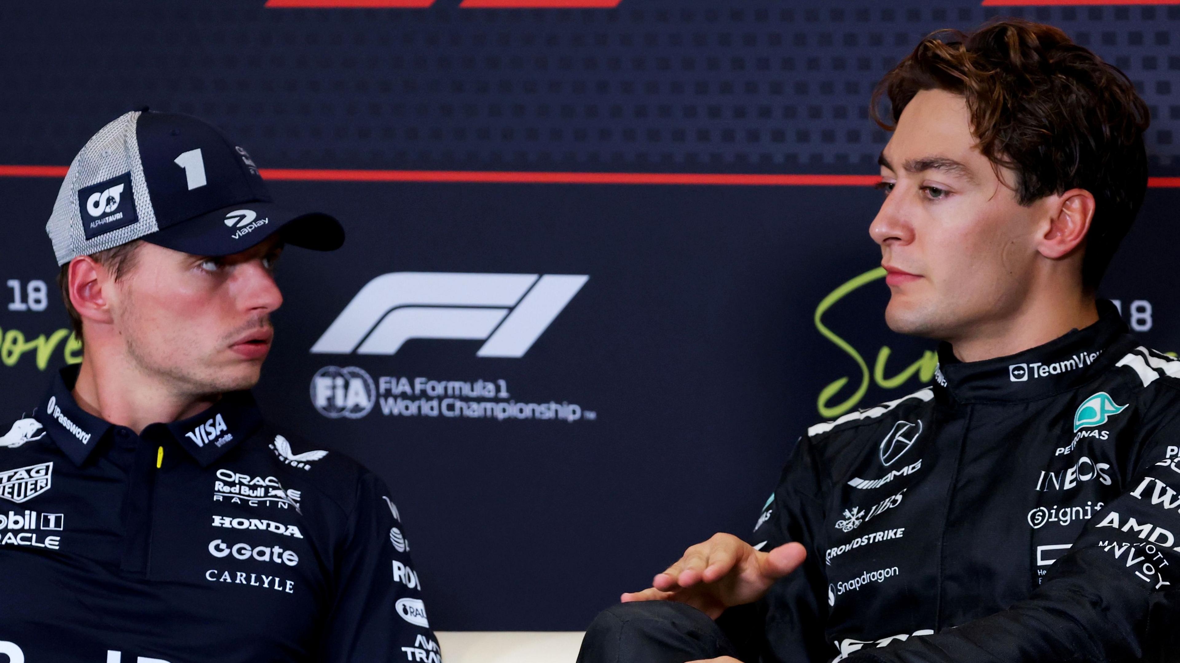 George Russell speaking to Max Verstappen at an FIA-F1 news conference during the 2025 Singapore Grand Prix
