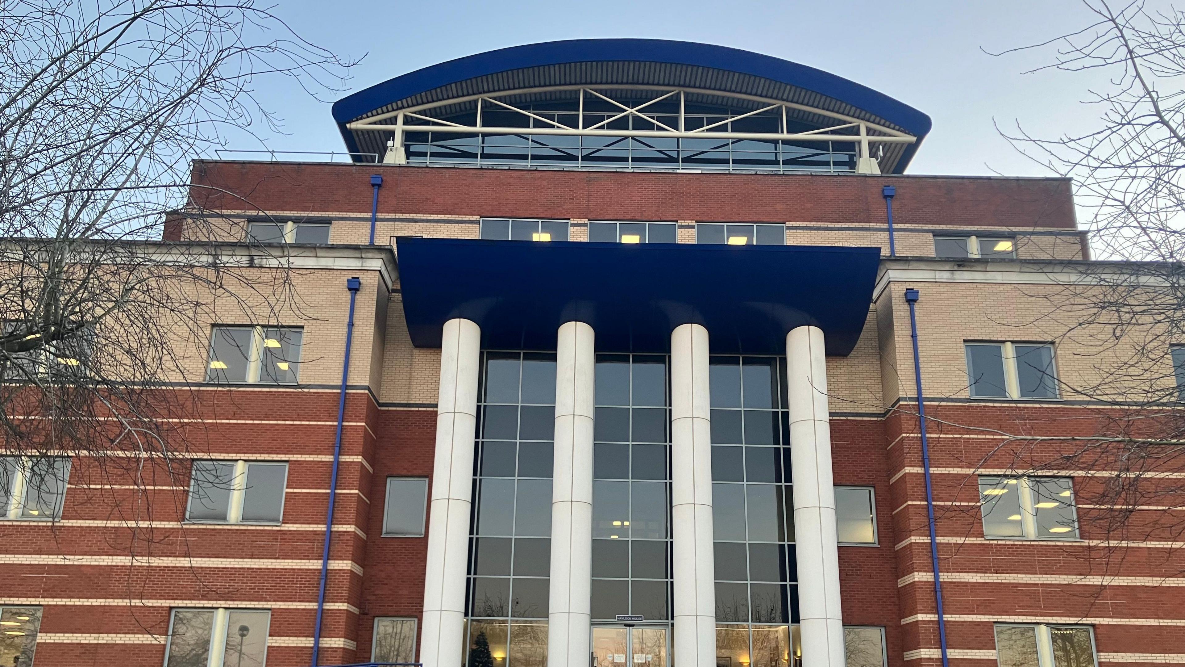 A red brick building with a glass entrance and four white columns at the front of the structure. 