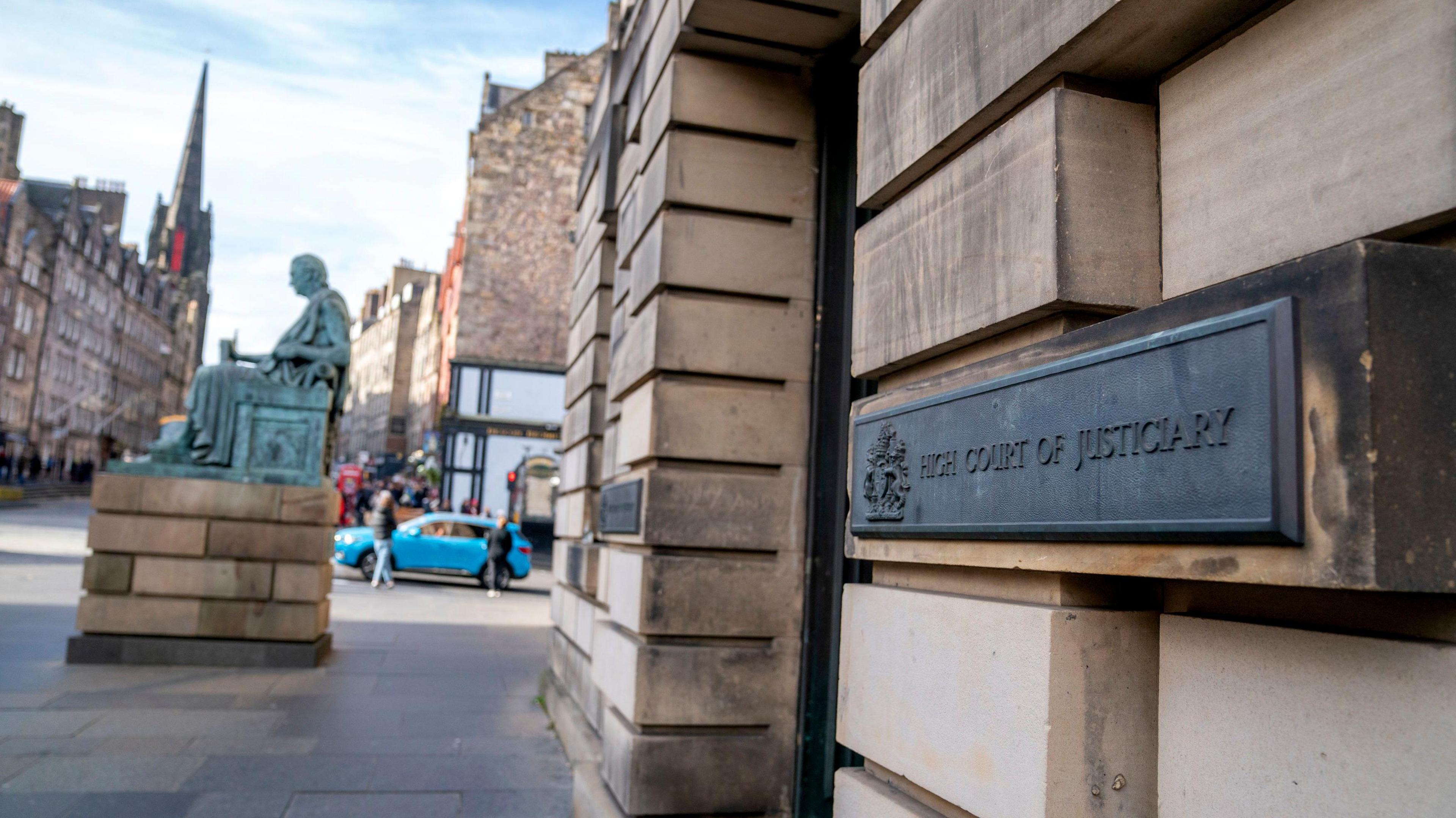 A general view of the outside of the High Court in Edinburgh. It is a stone building and the view is looking up the street to a statue and other buildings
