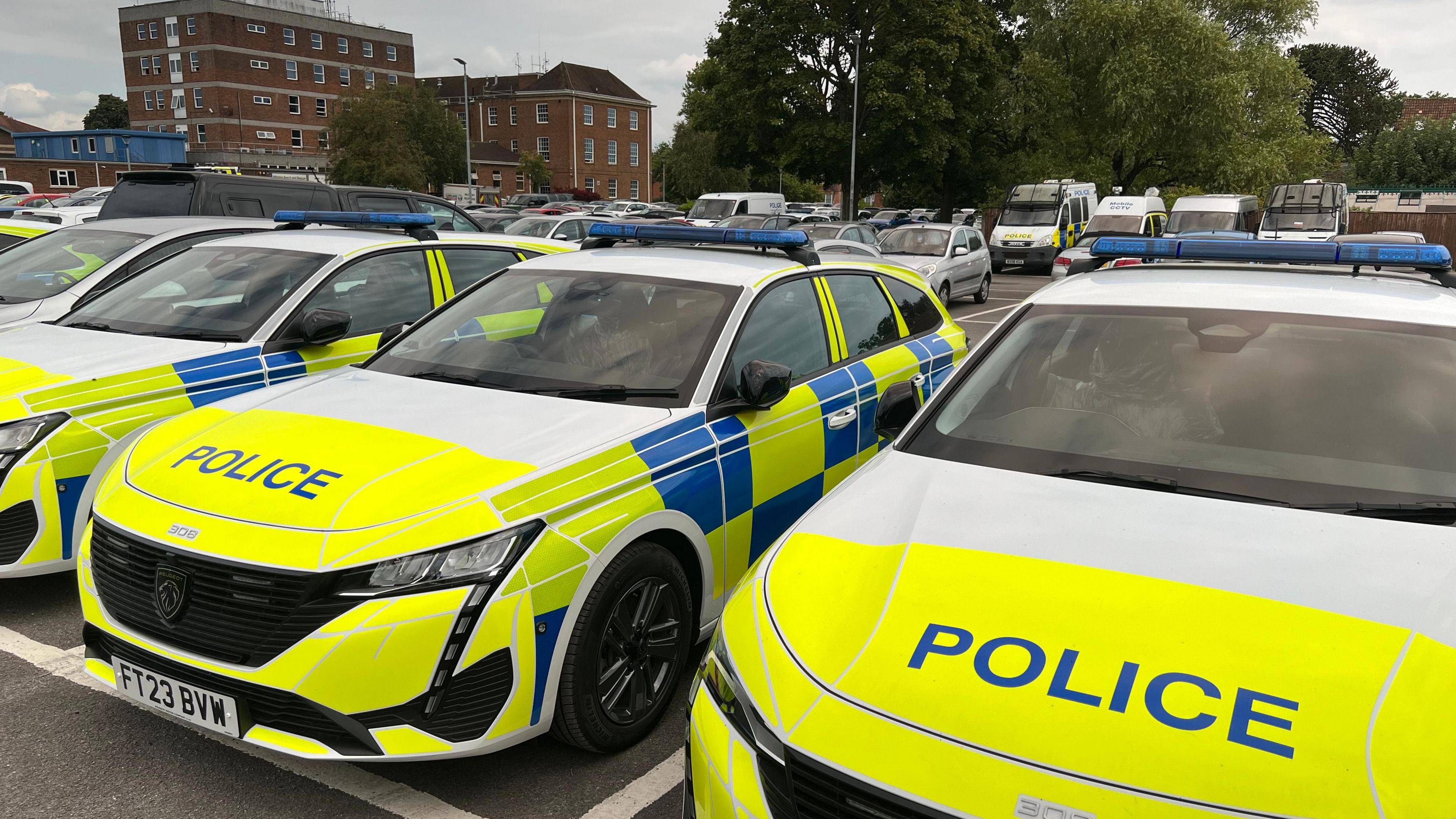 Police cars outside Devizes HQ. They are white with blue patterns and "police" written in blue lettering on their bonnets