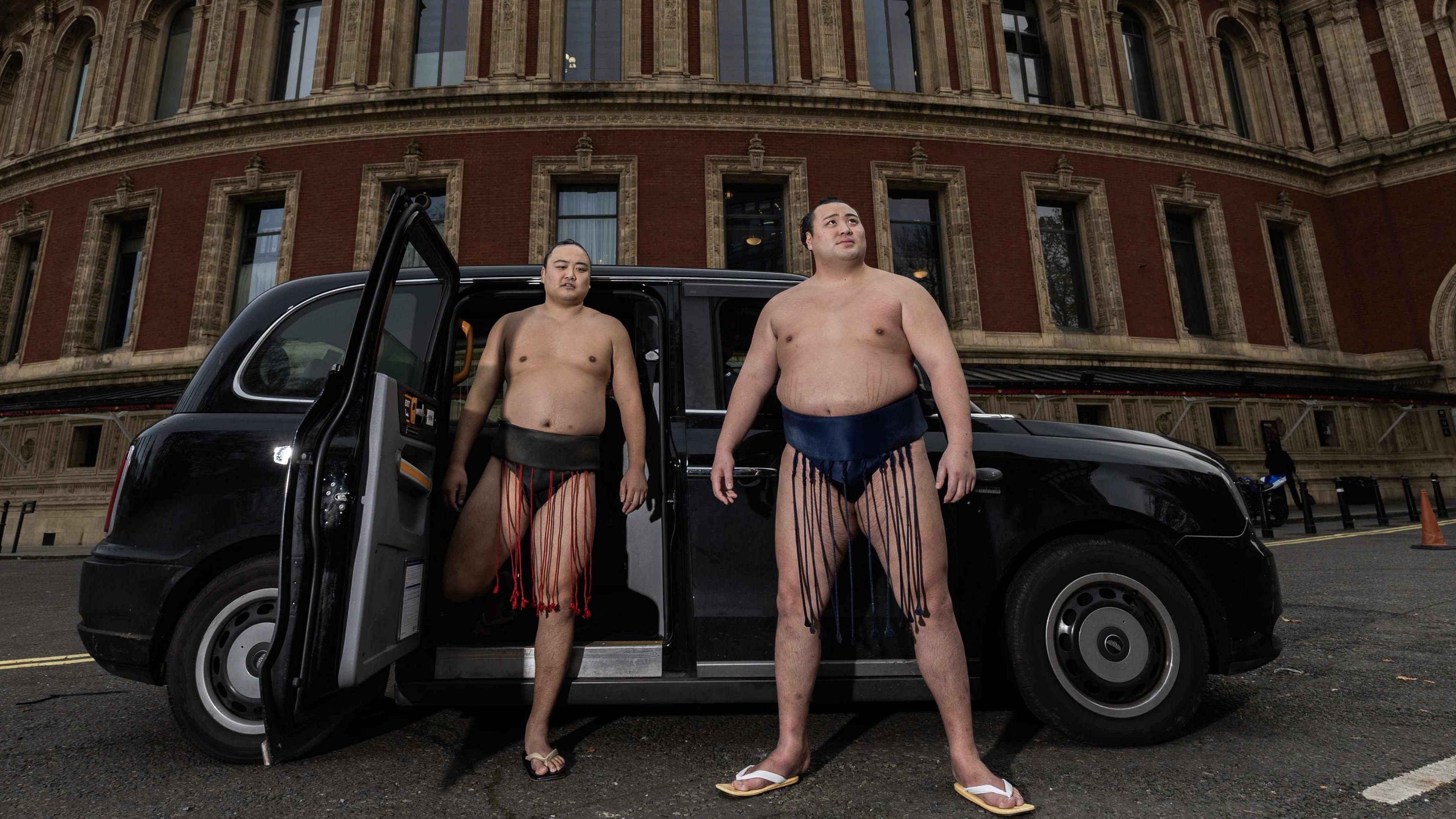 Two sumo wrestlers standing outside a black cab in front of the Royal Albert Hall