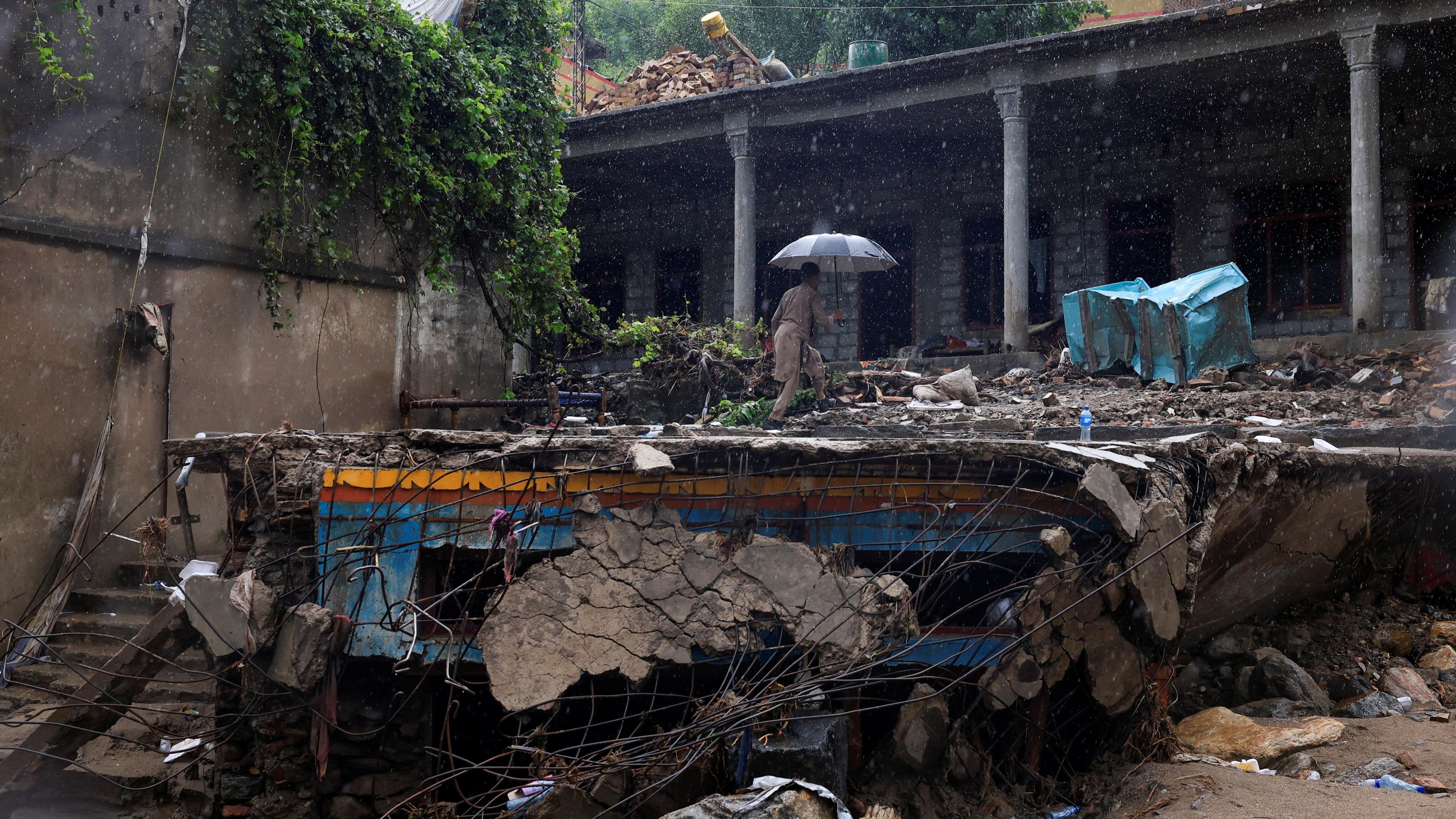 A resident walks with an umbrella to avoid rain at the damaged house, following a storm that caused heavy rains and flooding in Bayshonai Kalay, in Buner district, in Khyber Pakhtunkhwa province, Pakistan, August 18, 2025