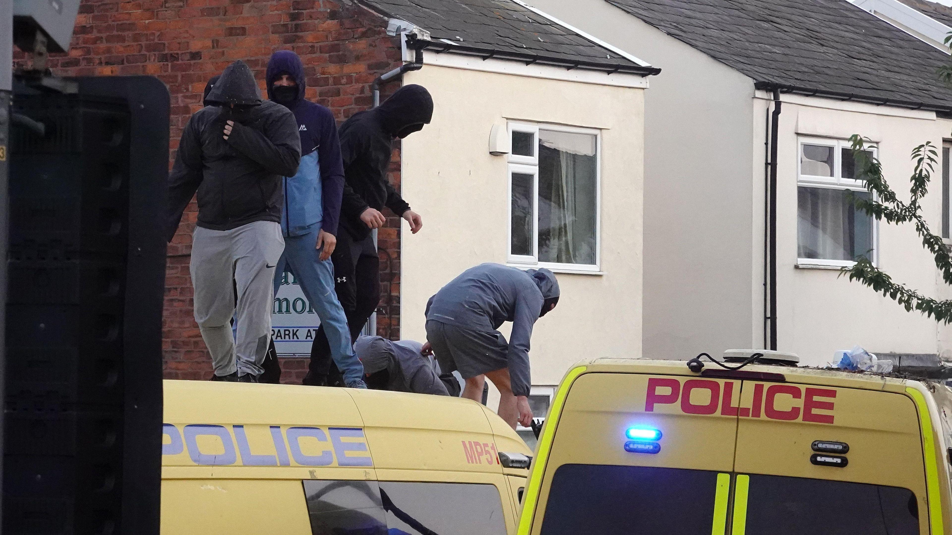 A group of men with face coverings stand on a police van during the Southport riot