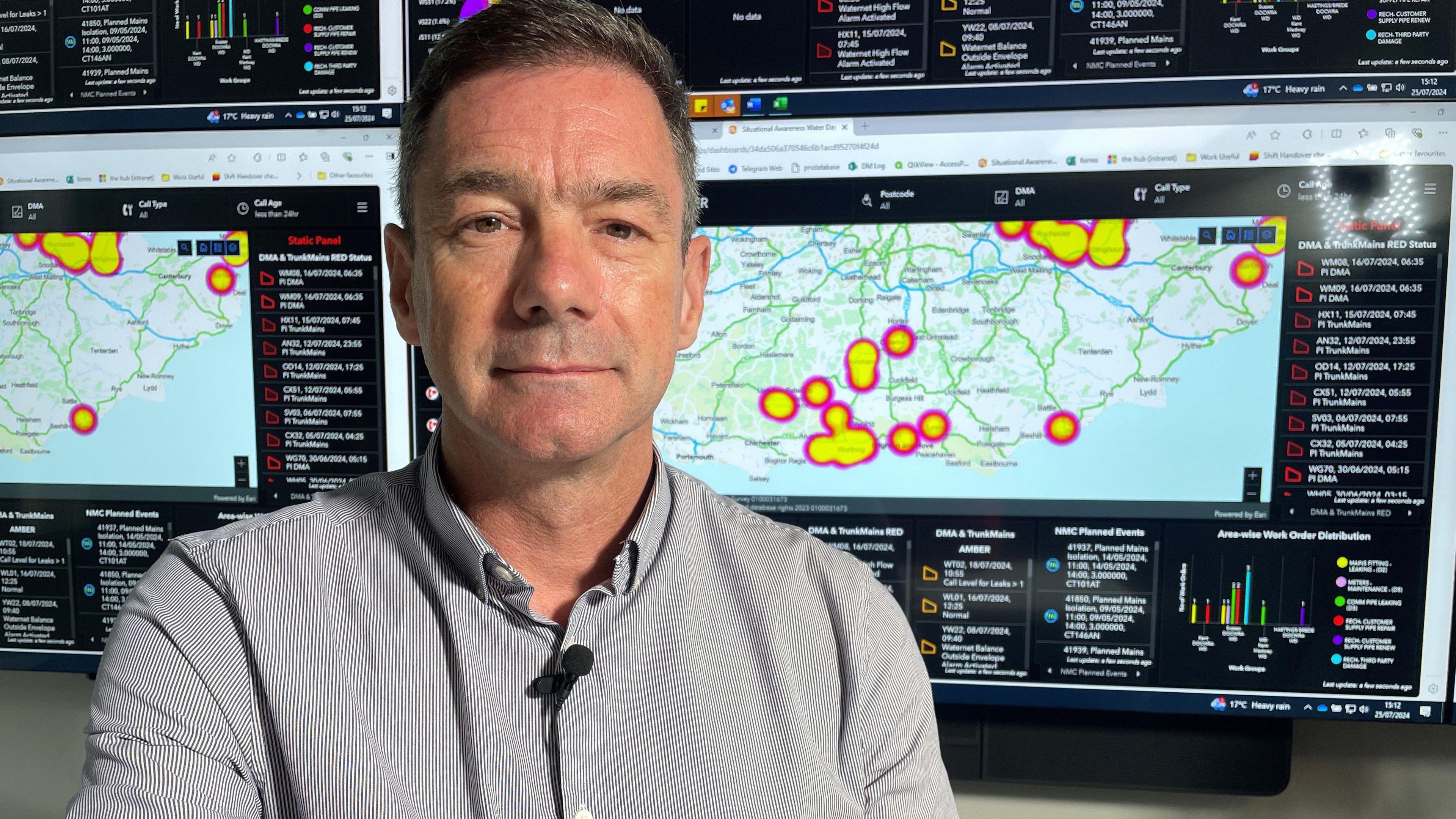 Lawrence Gosden in the control room of Southern Water with screens showing maps with yellow and red splodges in the background