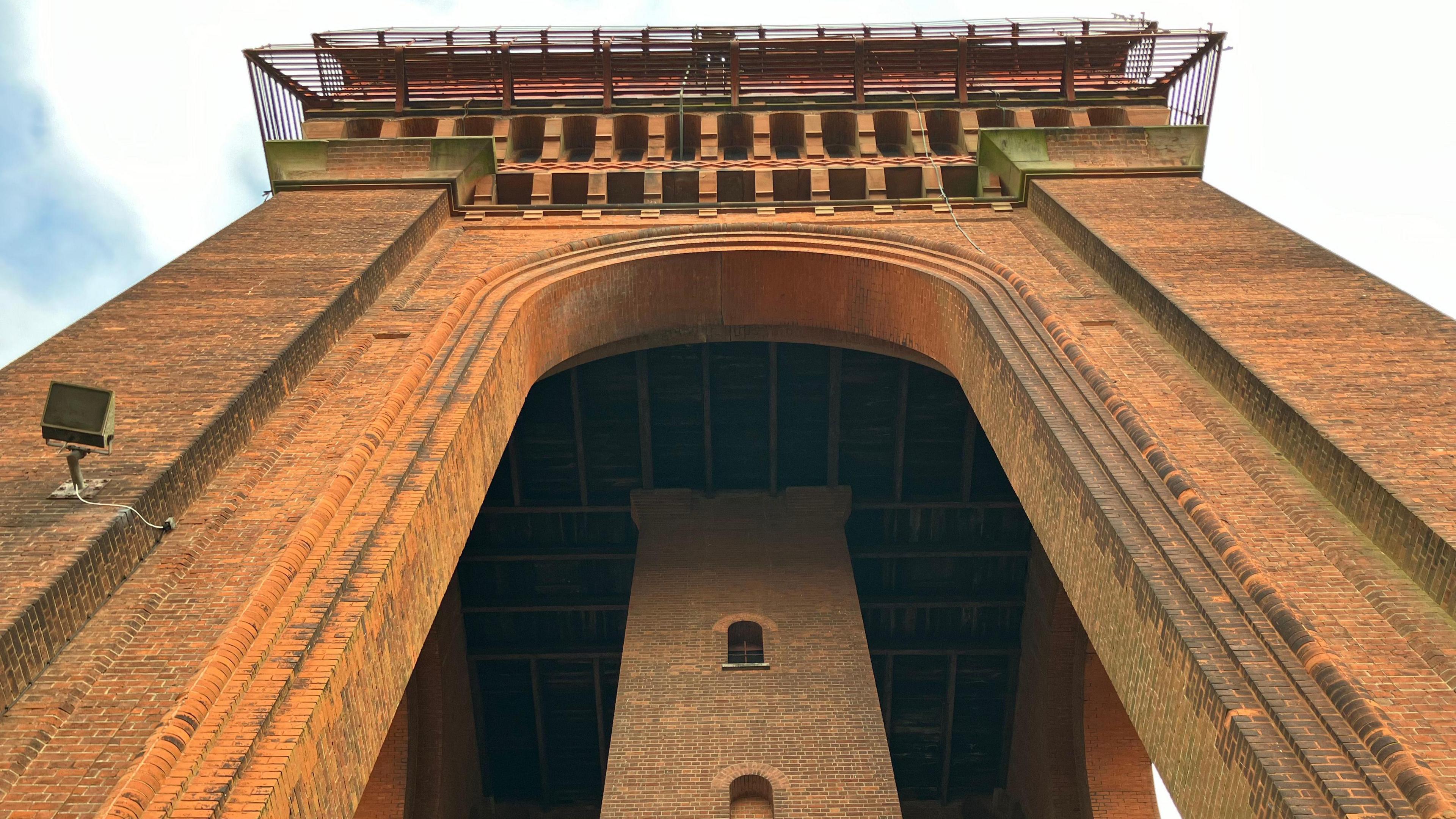 A large, red-brick water tower is pictured from below. An archway is visible, as is the side of a cast-iron tank which is now disused.