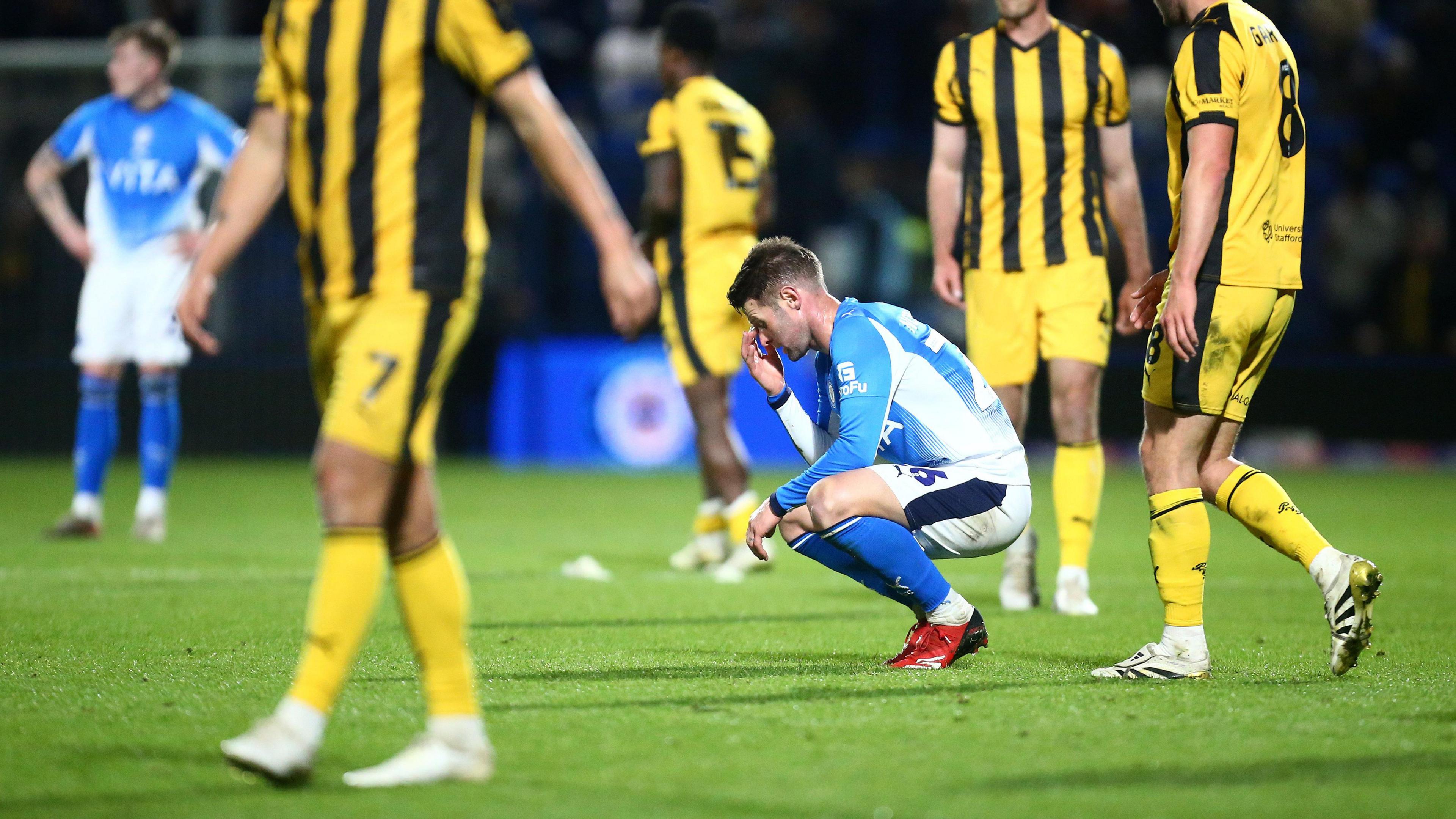 Stockport's Oliver Norwood crouches down in disappointment amongst Port Vale players after 2-1 loss