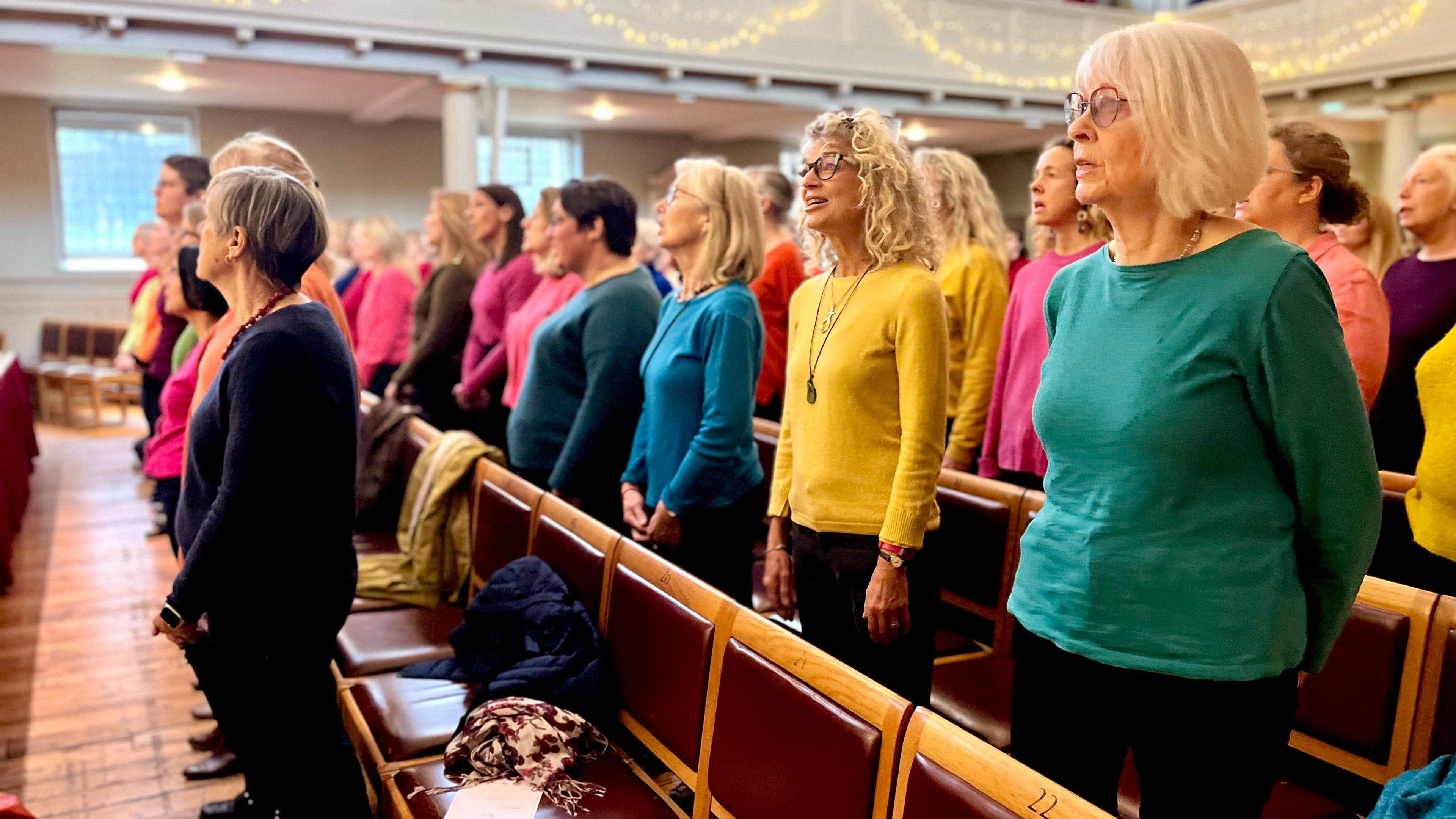 A group of people wearing colourful tops singing together but from another angle