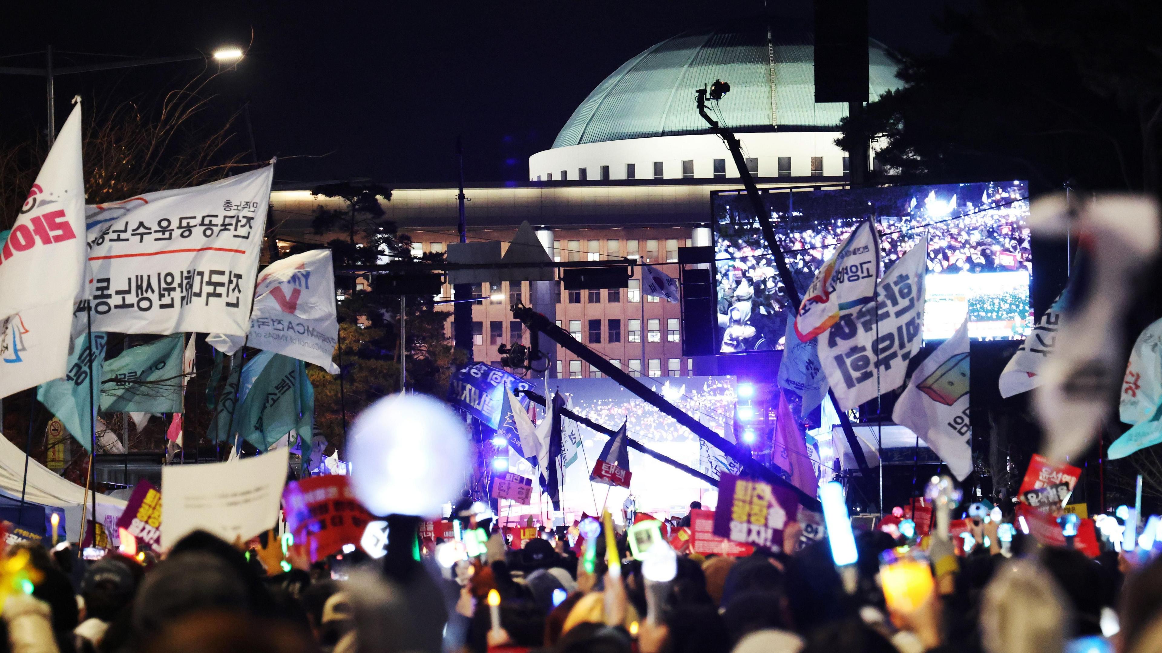 Protesters hold candlelights and wave flags during a demonstration outside the South Korea national assembly. There is a festival atmosphere.