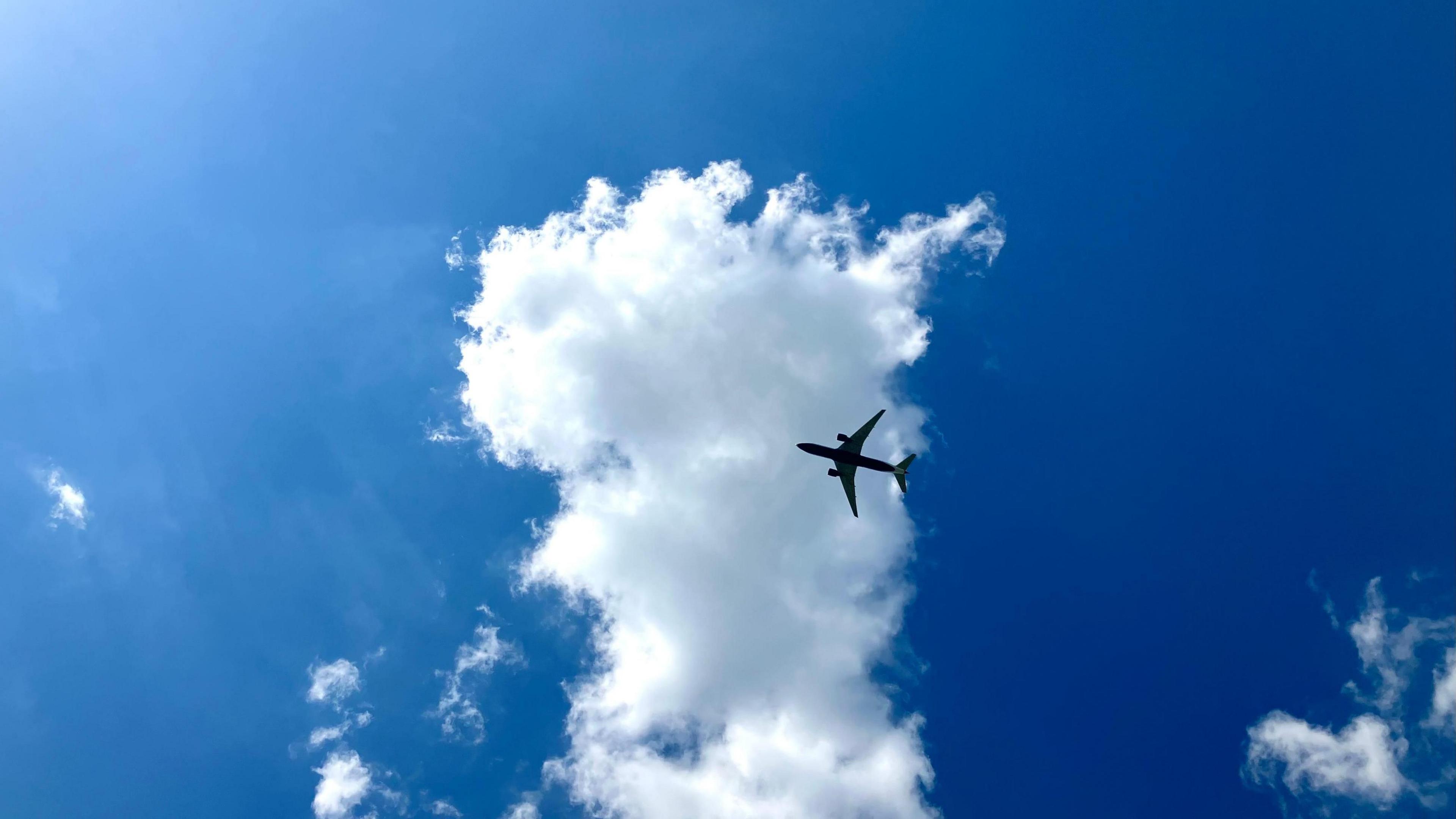 A jet plane with two engines flies in front of a white cloud with a blue sky in the background