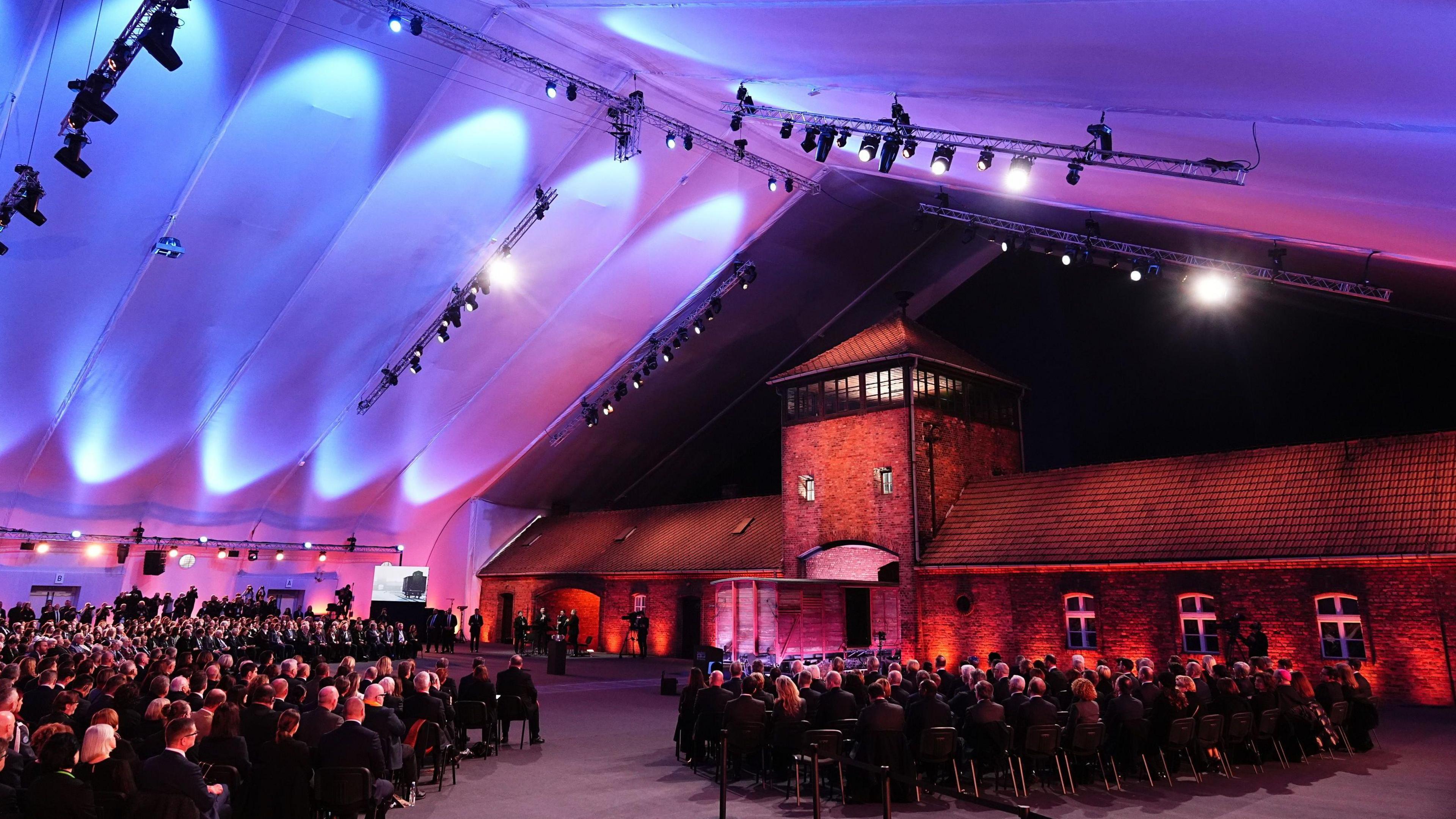 A service being held at Auschwitz-Birkenau which is lit up by purple lights.