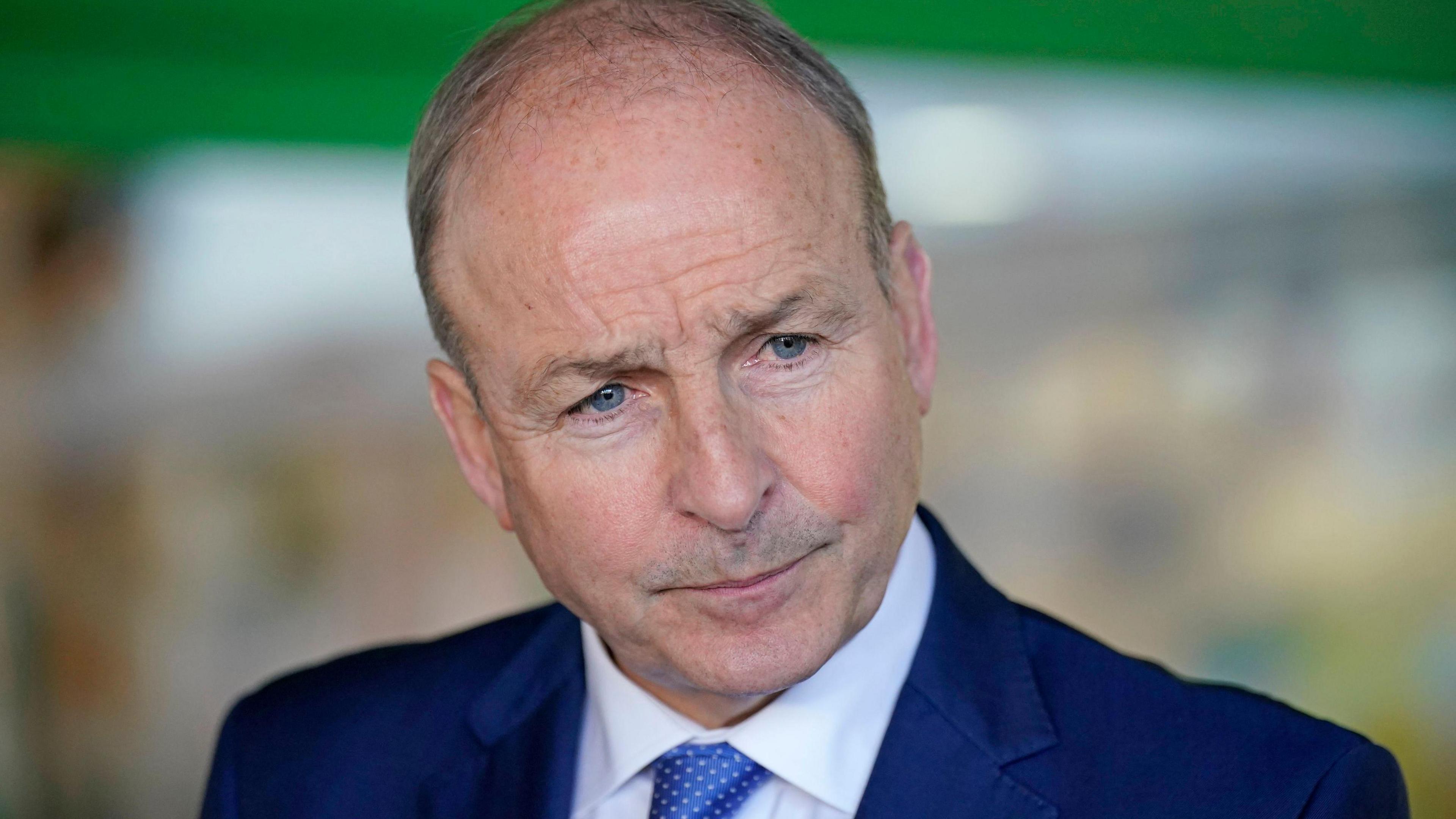 Micheal Martin wearing white shirt, blue tie and blue jacket stares ahead waiting to answer questions from the media