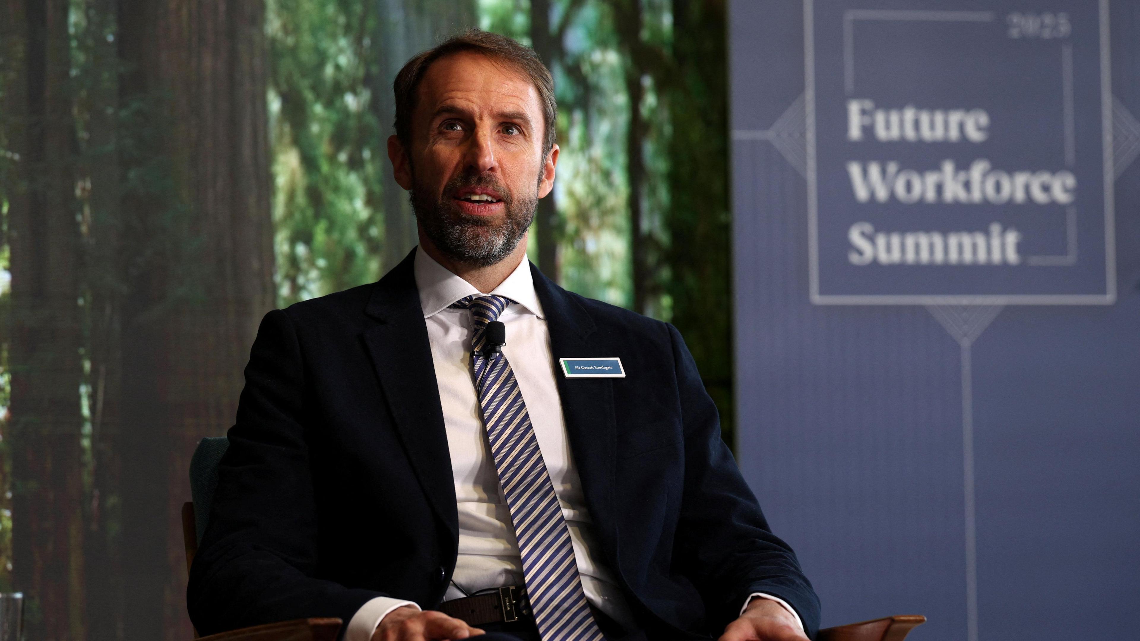Sir Gareth Southgate wearing a suit and tie, sitting on a chair in front of a backdrop which reads "Future Workforce Summit"