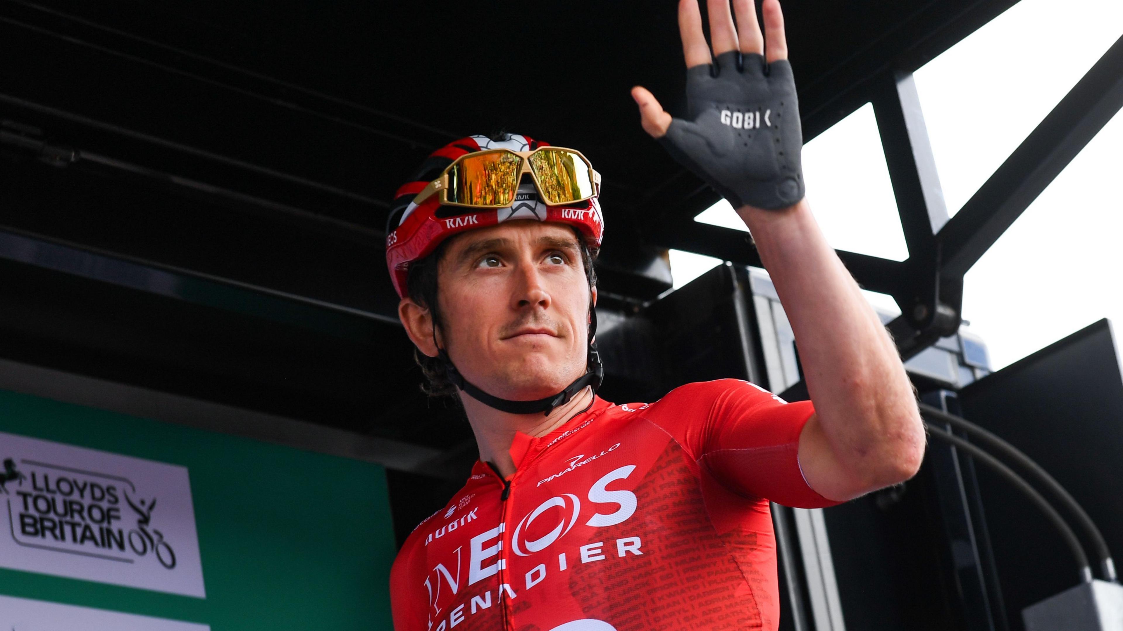 Geraint Thomas wears a red helmet and jersey as he waves