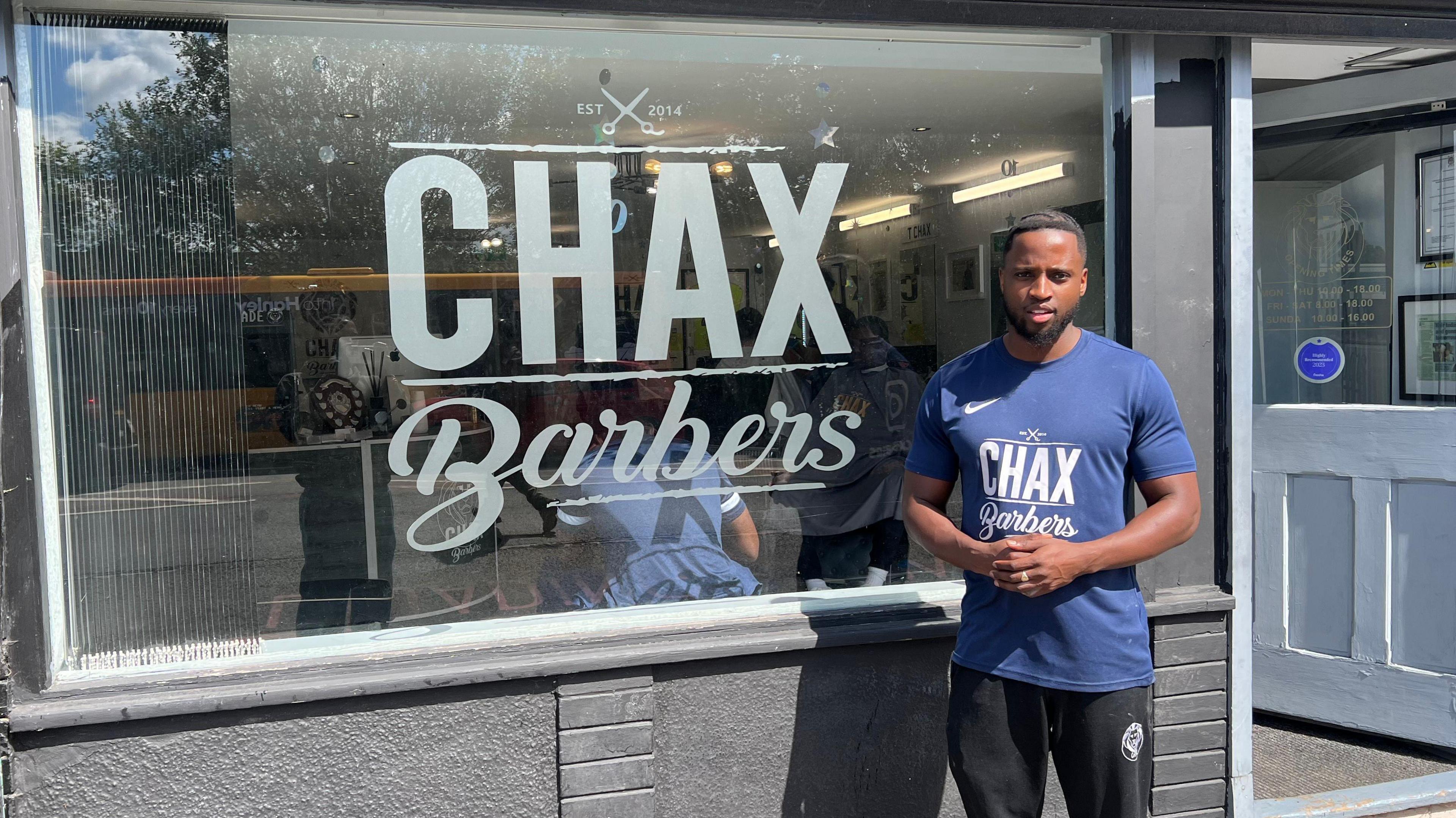 Leeroy Chax standing outside his barbers shop. He is wearing a blue T-shirt.