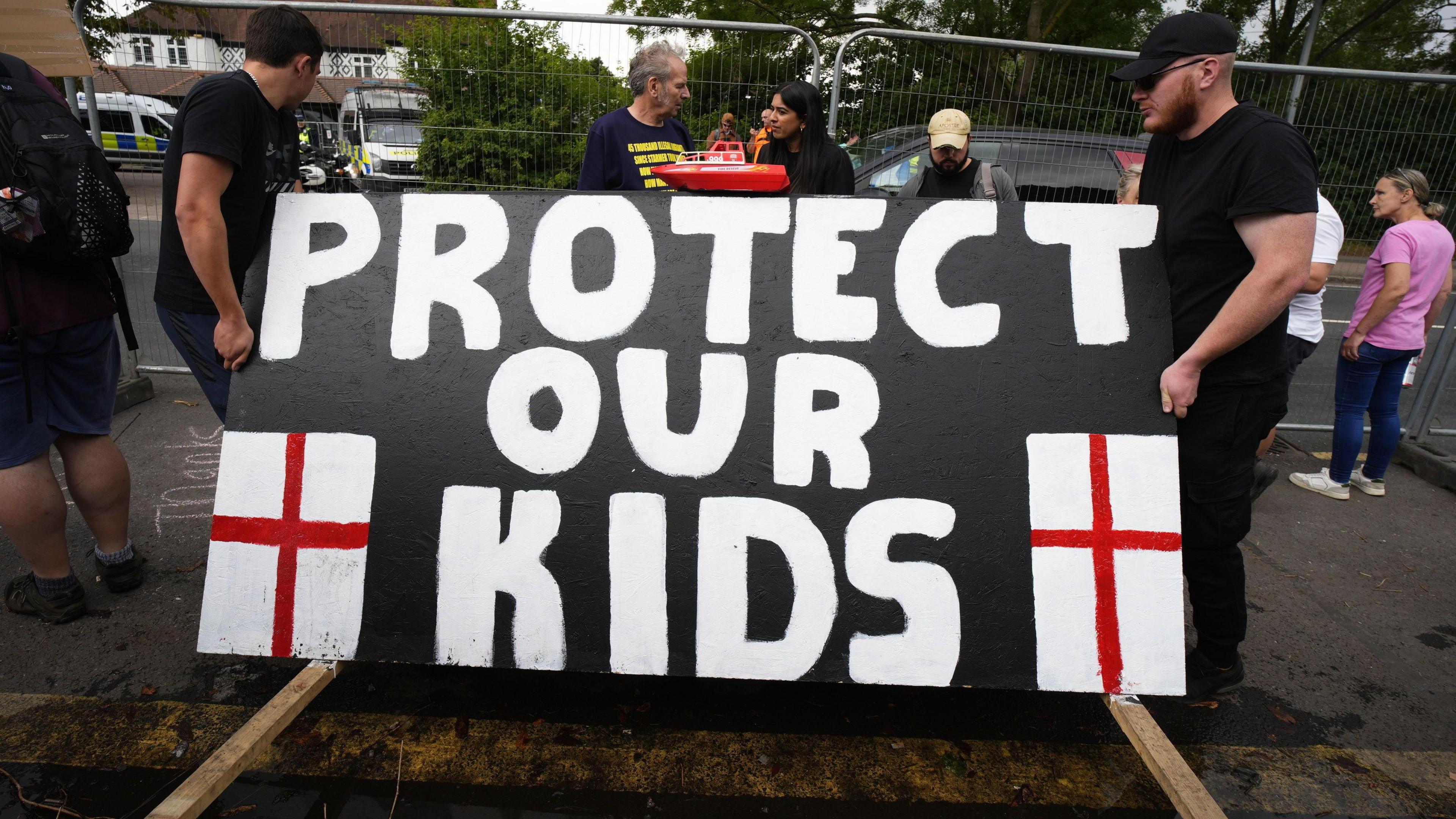 Two men holding a big placard that reads "Protect our kids".