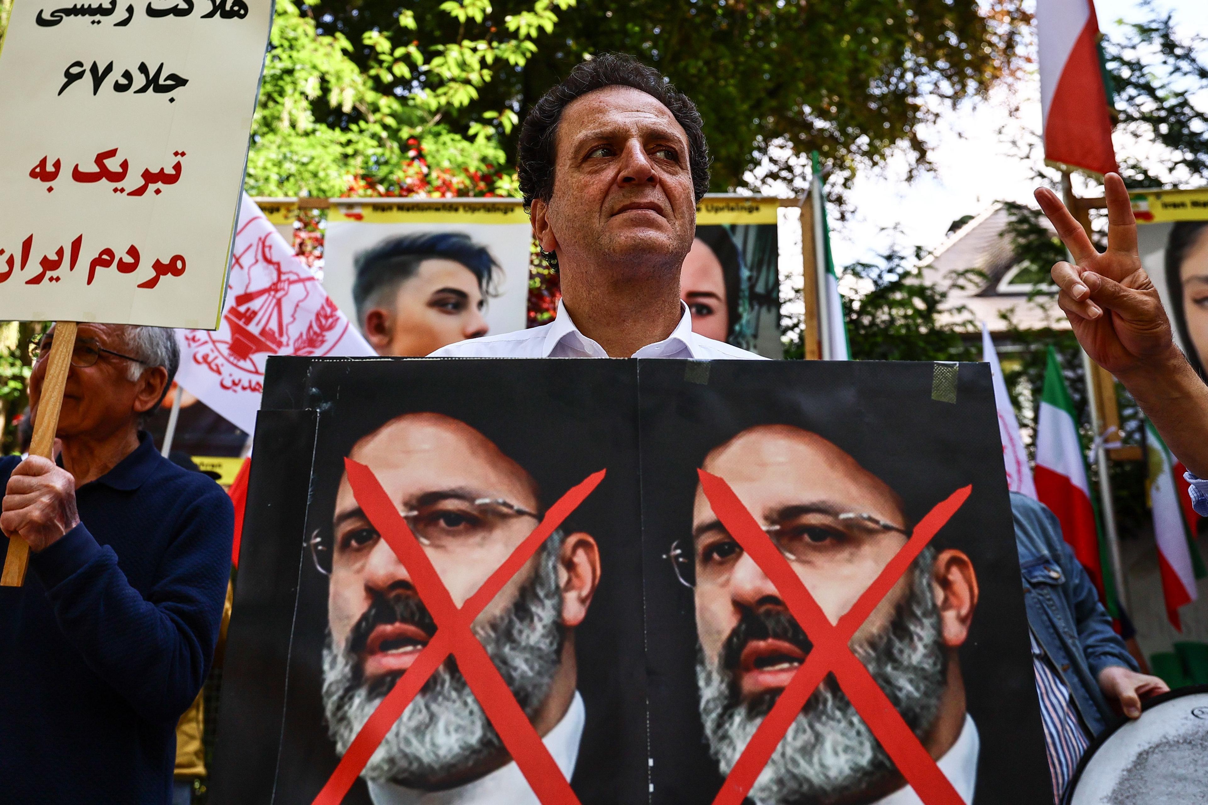 Protesters in Berlin following the death of the death of President Raisi. A man stands with a poster, showing two faces of Raisi with red crosses through them