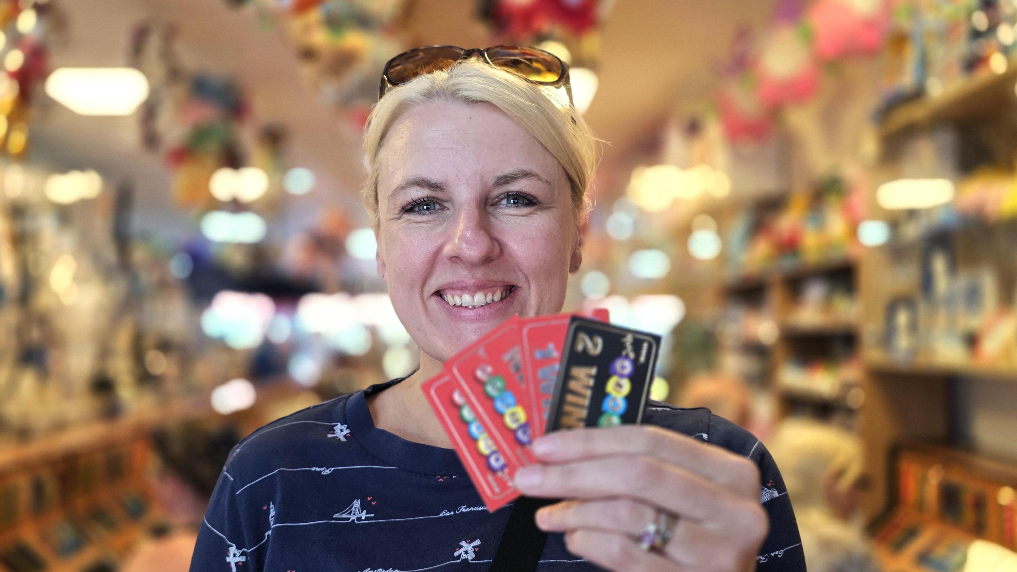We can see a smiling Michelle Fitzgerald. She has a dark blue top on with white stripes across. She's holding four winning bingo tickets.