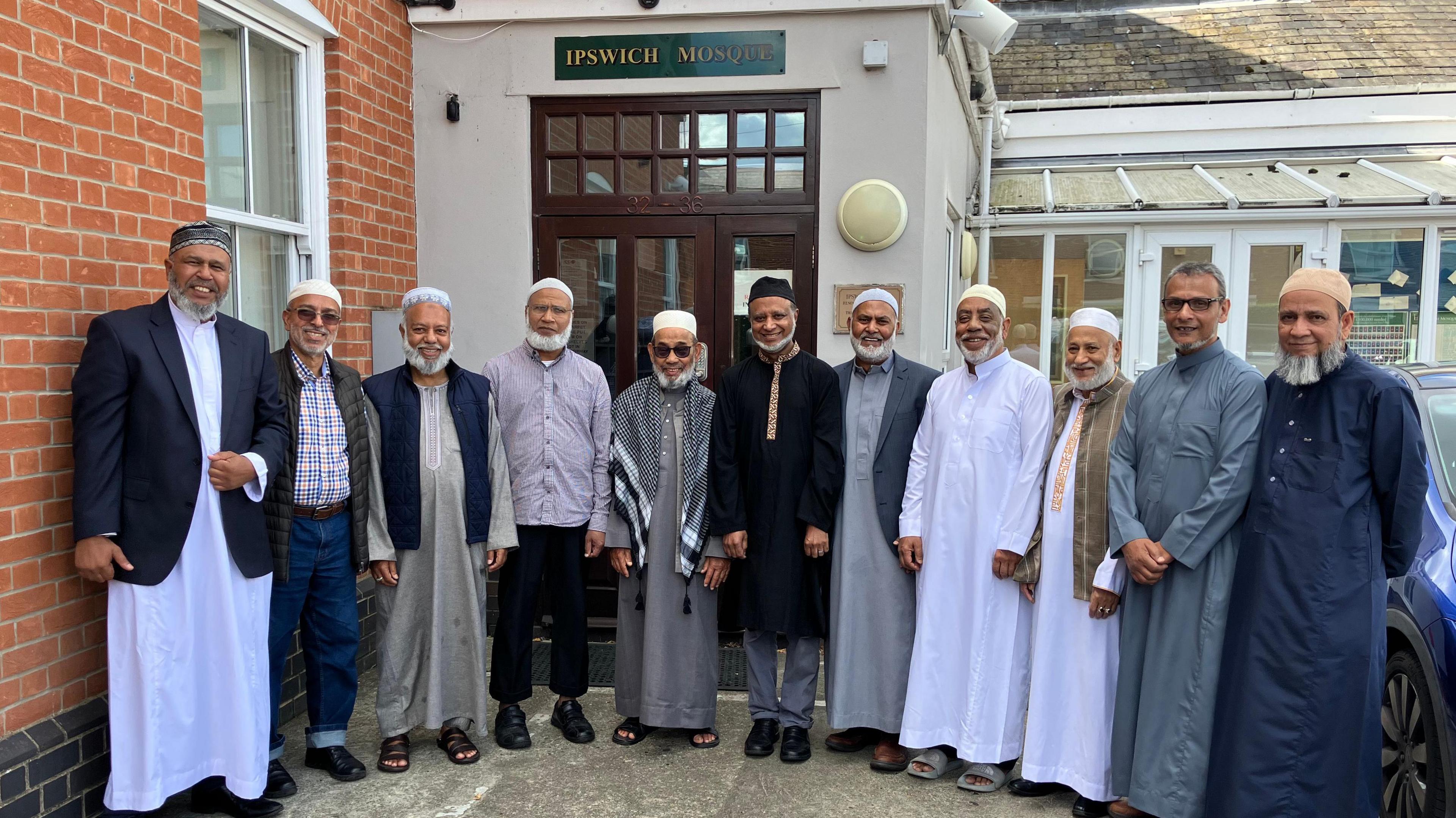 11 men, mostly in traditional Muslim dress, stand in front of Ipswich mosque.
