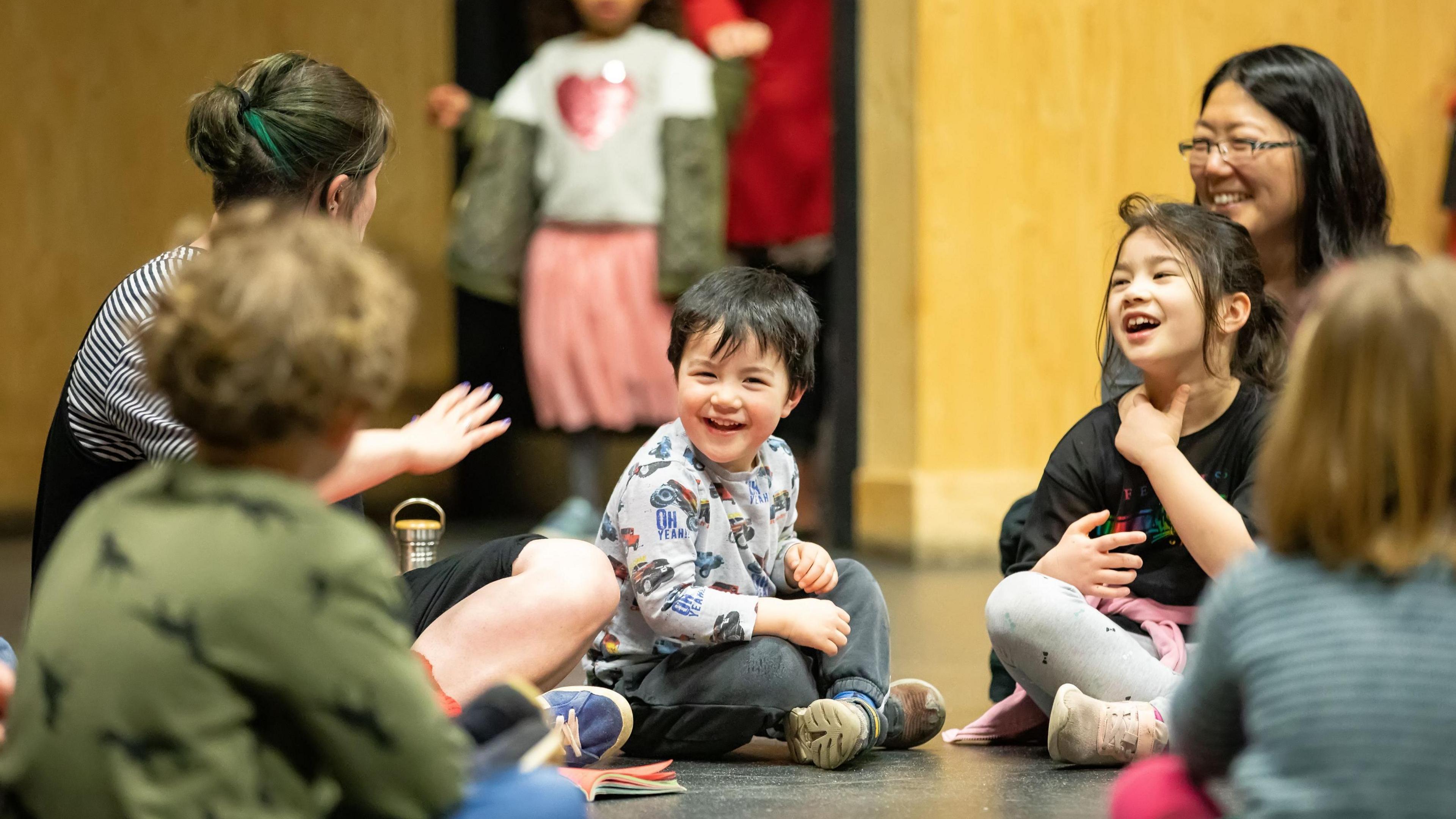 Children sat on the floor smiling and listening to group leader 